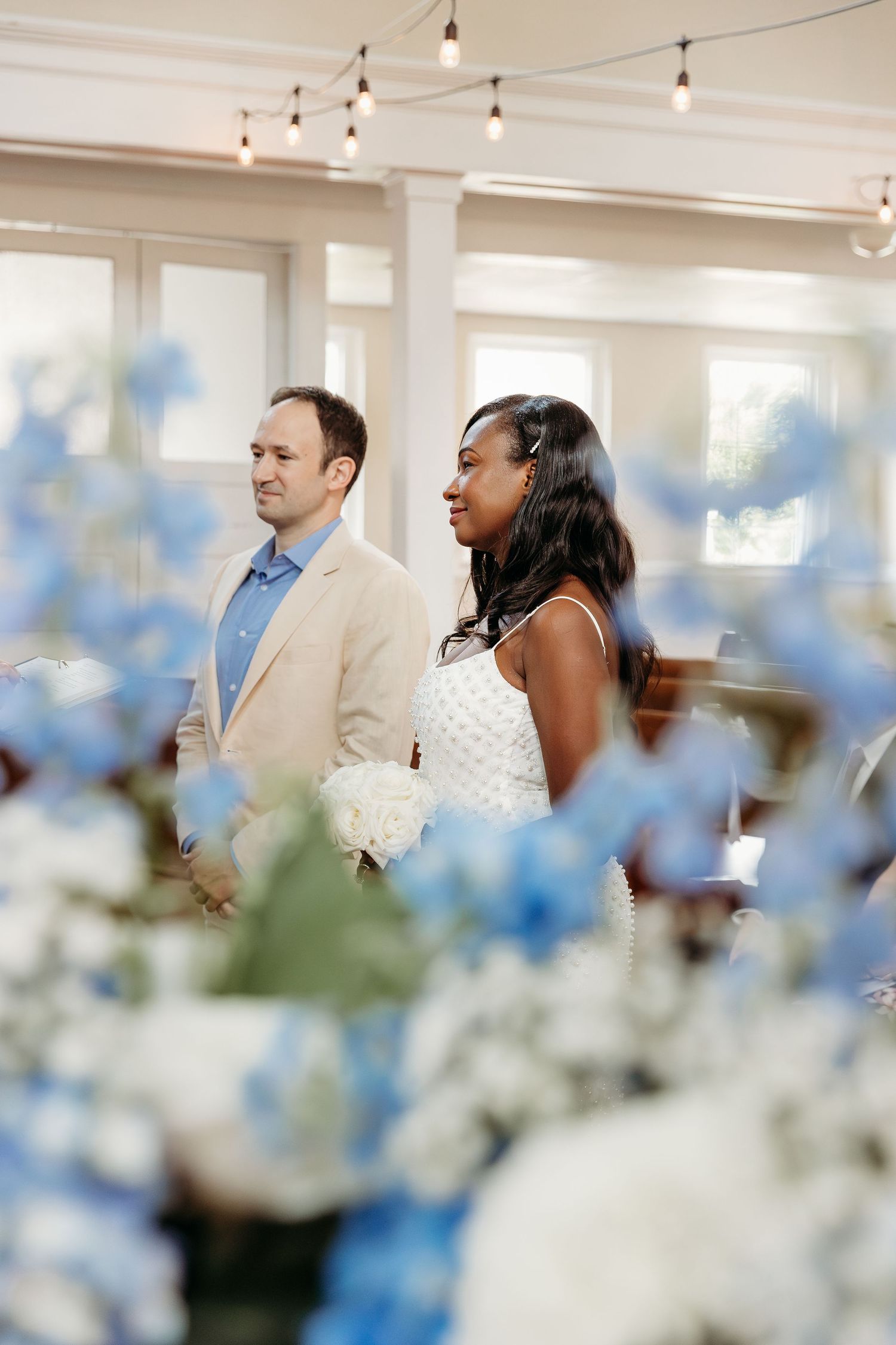 Wedding guests enjoy a celebration in an elegant white venue decorated with delicate blue and white flowers.