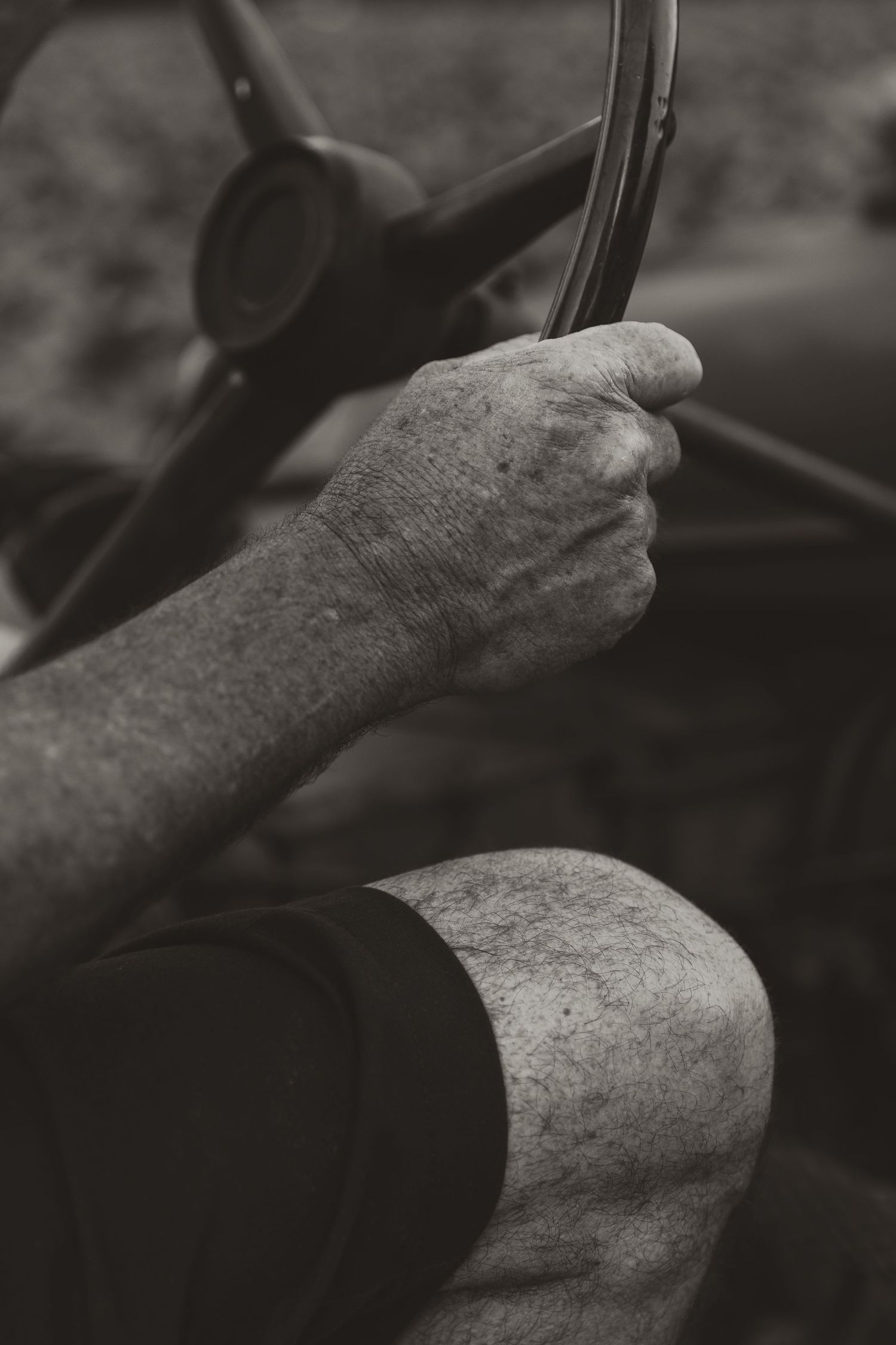 A black and white close-up photograph shows hands the wheel of a vintage tractor