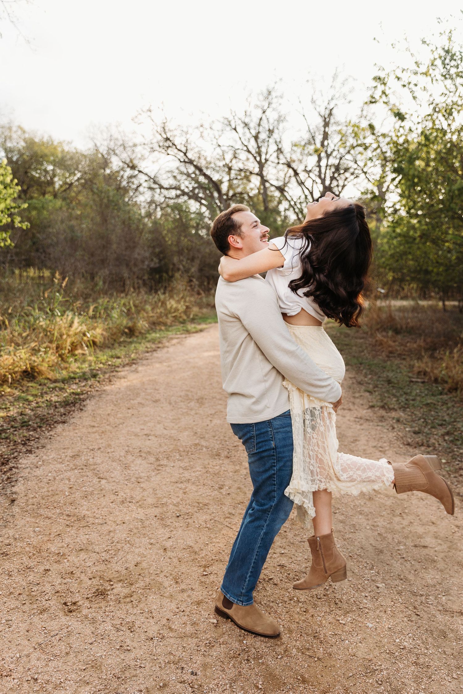A couple dances and spins together on a dirt path surrounded by autumn trees and brush.