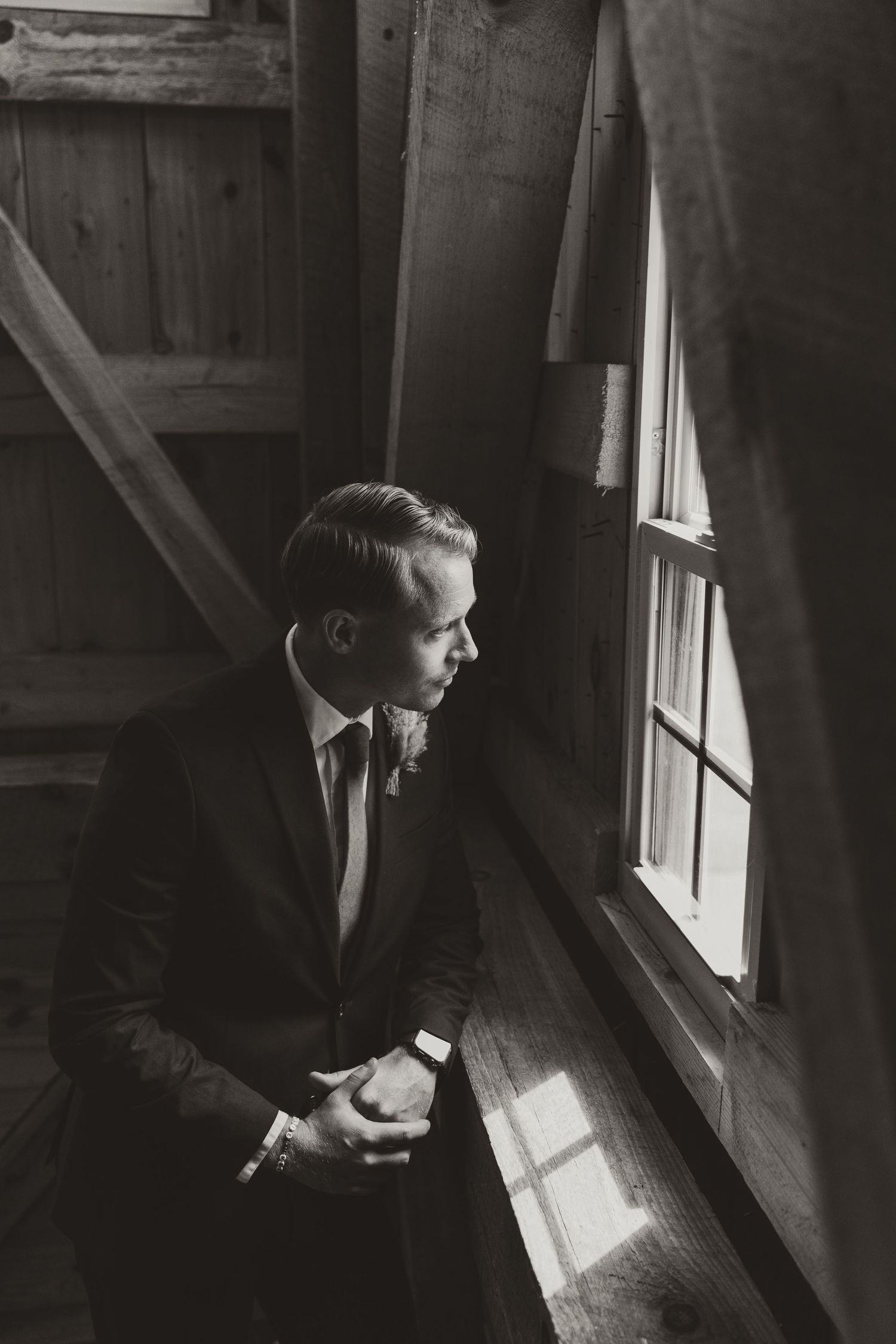 A contemplative figure in a suit gazes through a window in dramatic black and white lighting.
