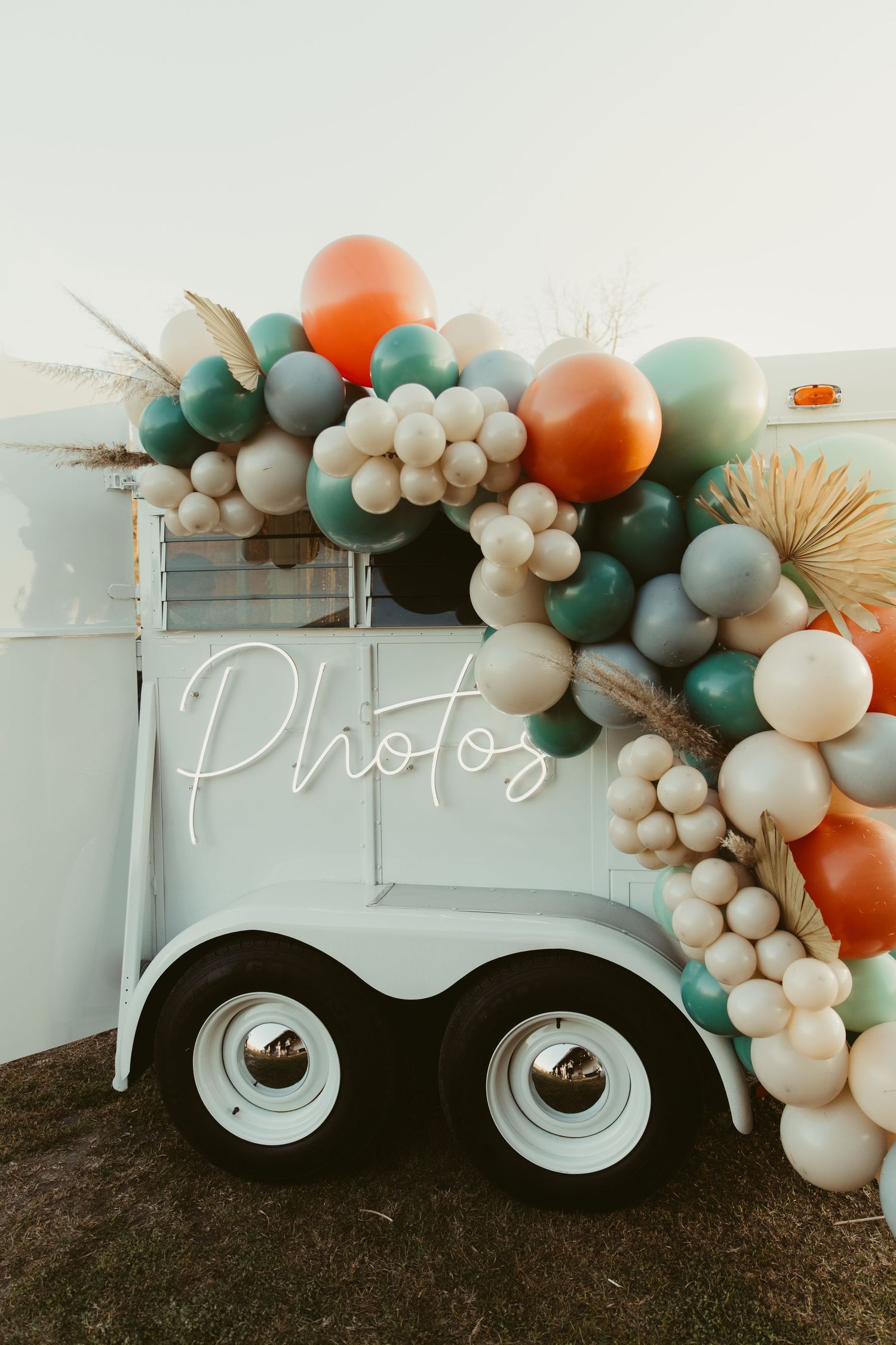 Vintage photo booth trailer decorated with teal, orange and white balloon garland in modern boho style.