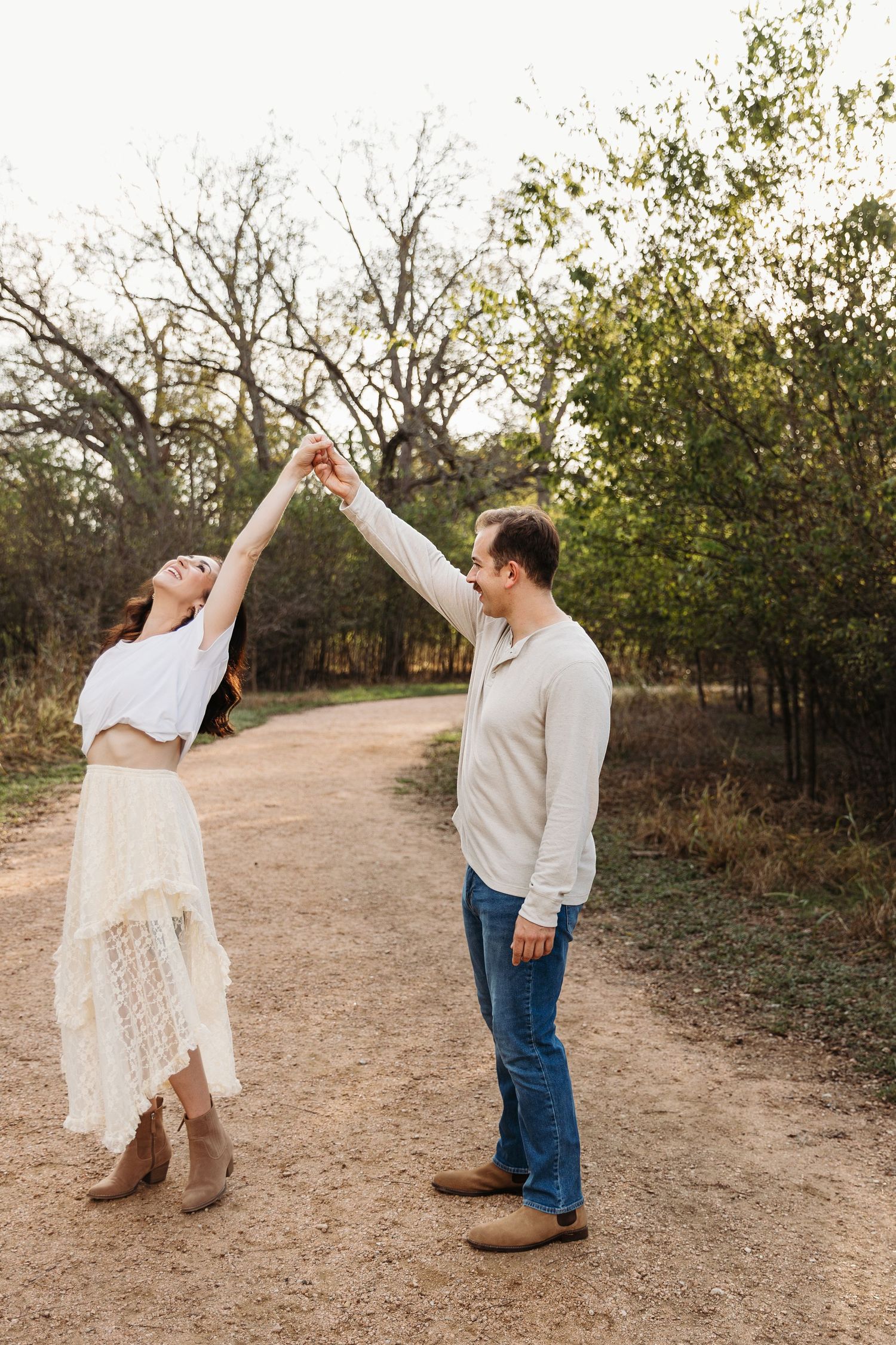 A couple dances together on a dirt path surrounded by autumn trees and bushes.