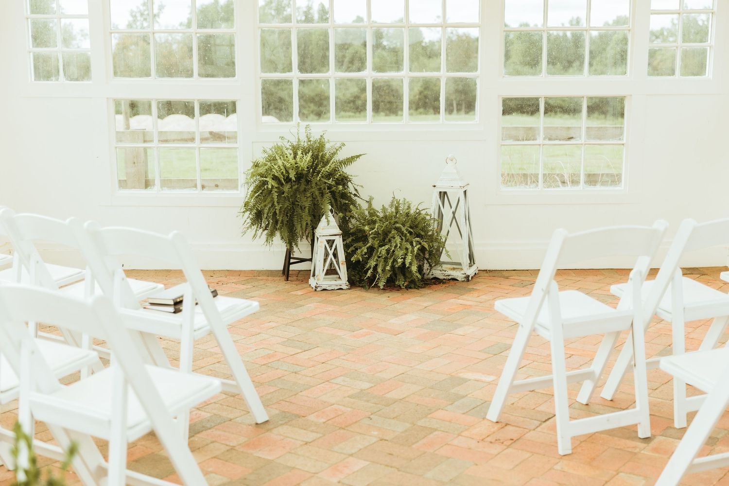 White wooden chairs line a brick patio surrounded by lush greenery and windows at a North Carolina wedding venue