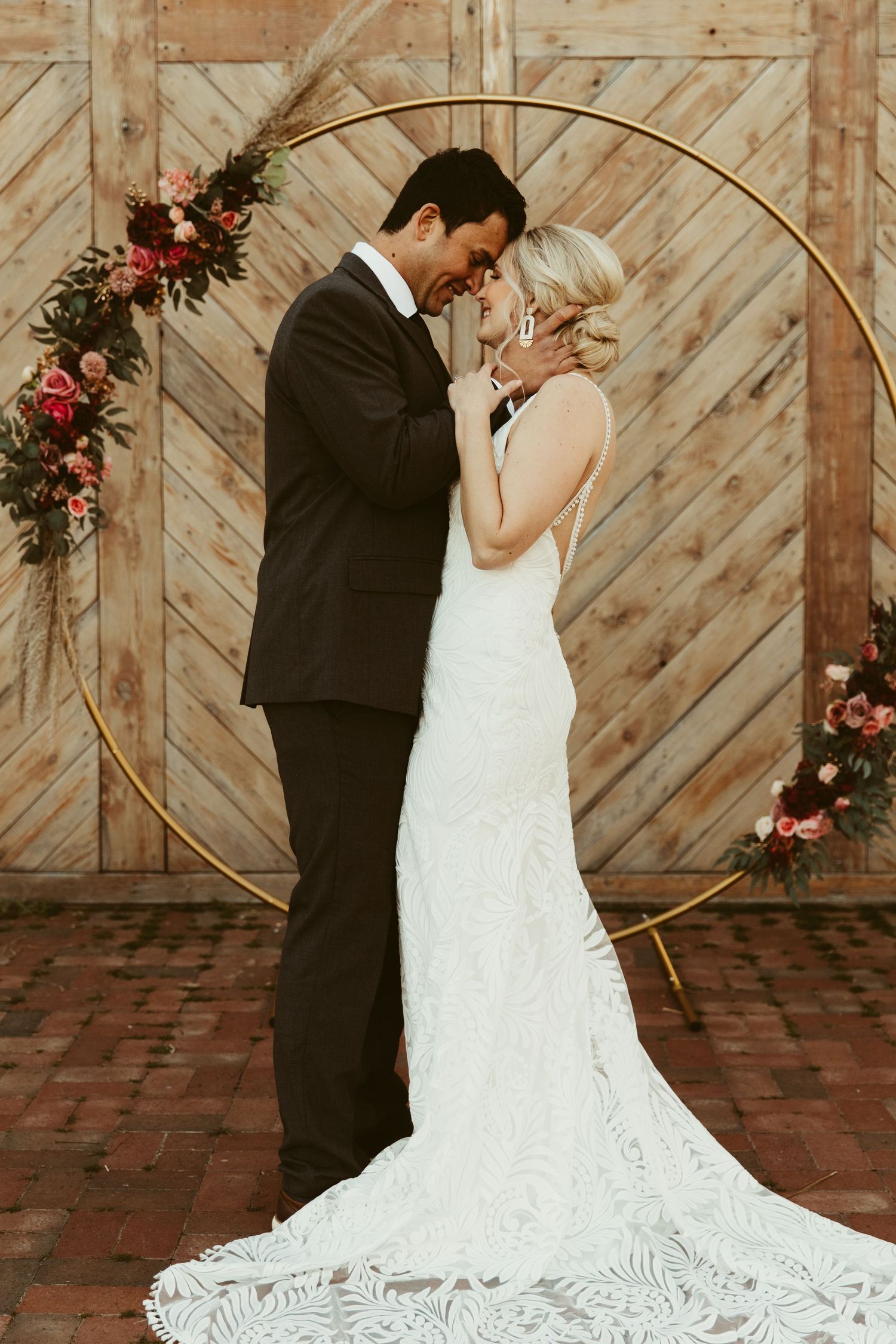 A romantic moment between newlyweds in front of a rustic wooden barn wall with floral decorations.
