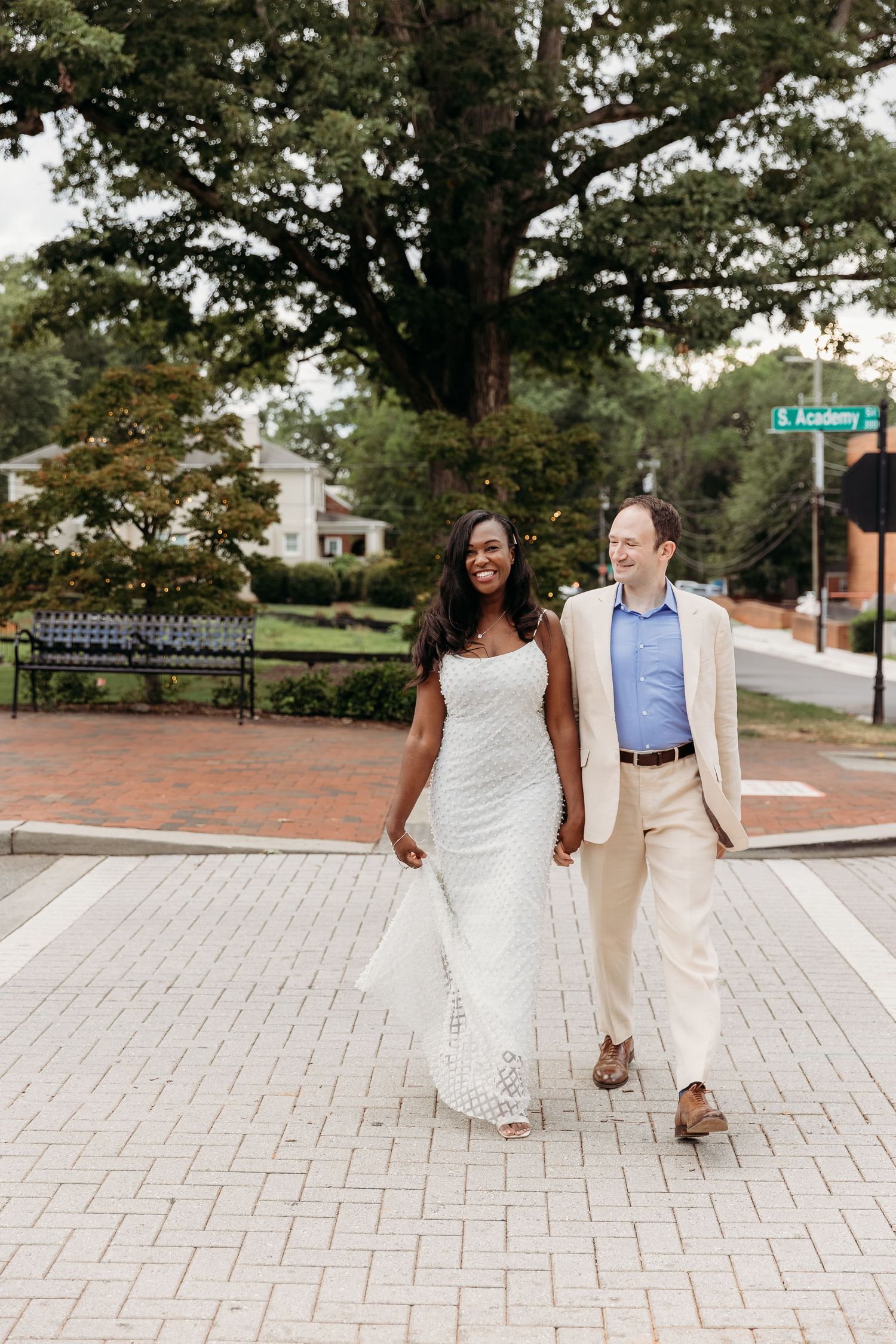 A couple walks together on a brick paved path while holding hands on a sunny day.