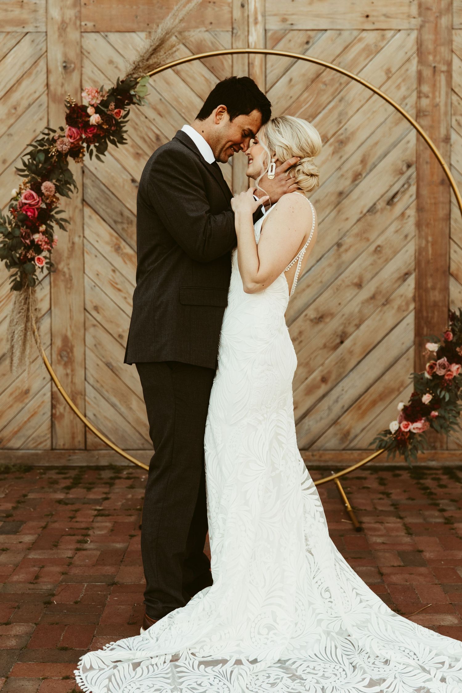 A romantic moment between newlyweds in front of a rustic wooden barn wall with floral decorations.