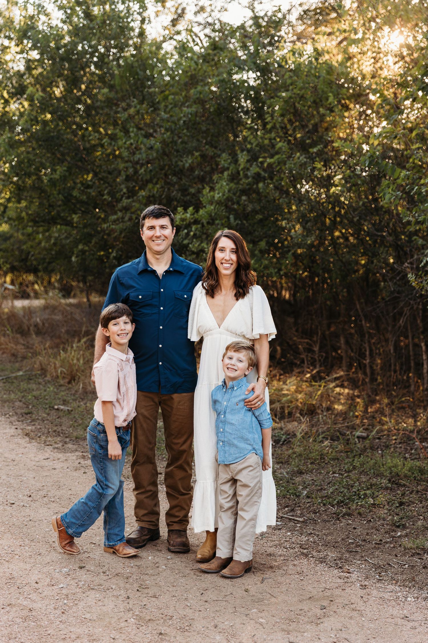 A family poses together on a dirt path at sunset with trees in the background.