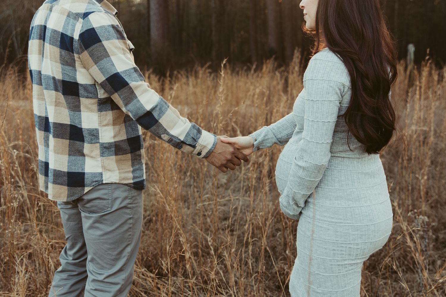 A couple in plaid shirt and mint dress embrace in a golden field during a maternity photo session.