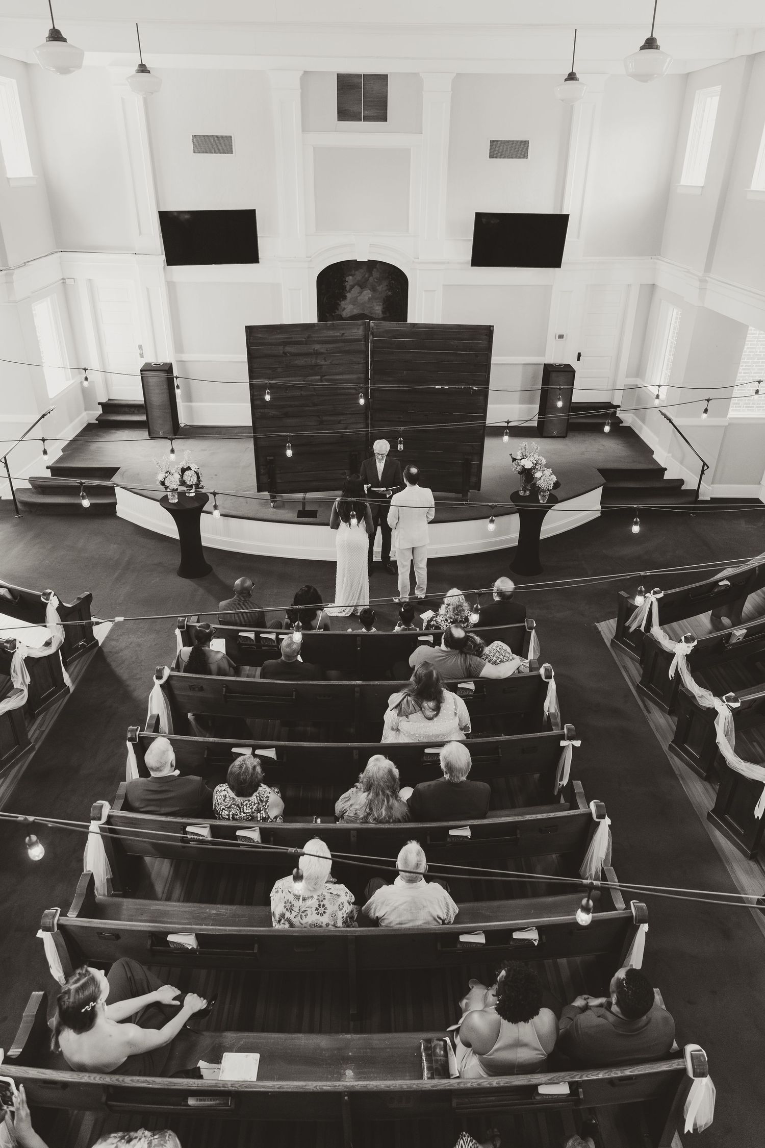 Black and white photo of people seated in curved wooden pews inside a historic church sanctuary.