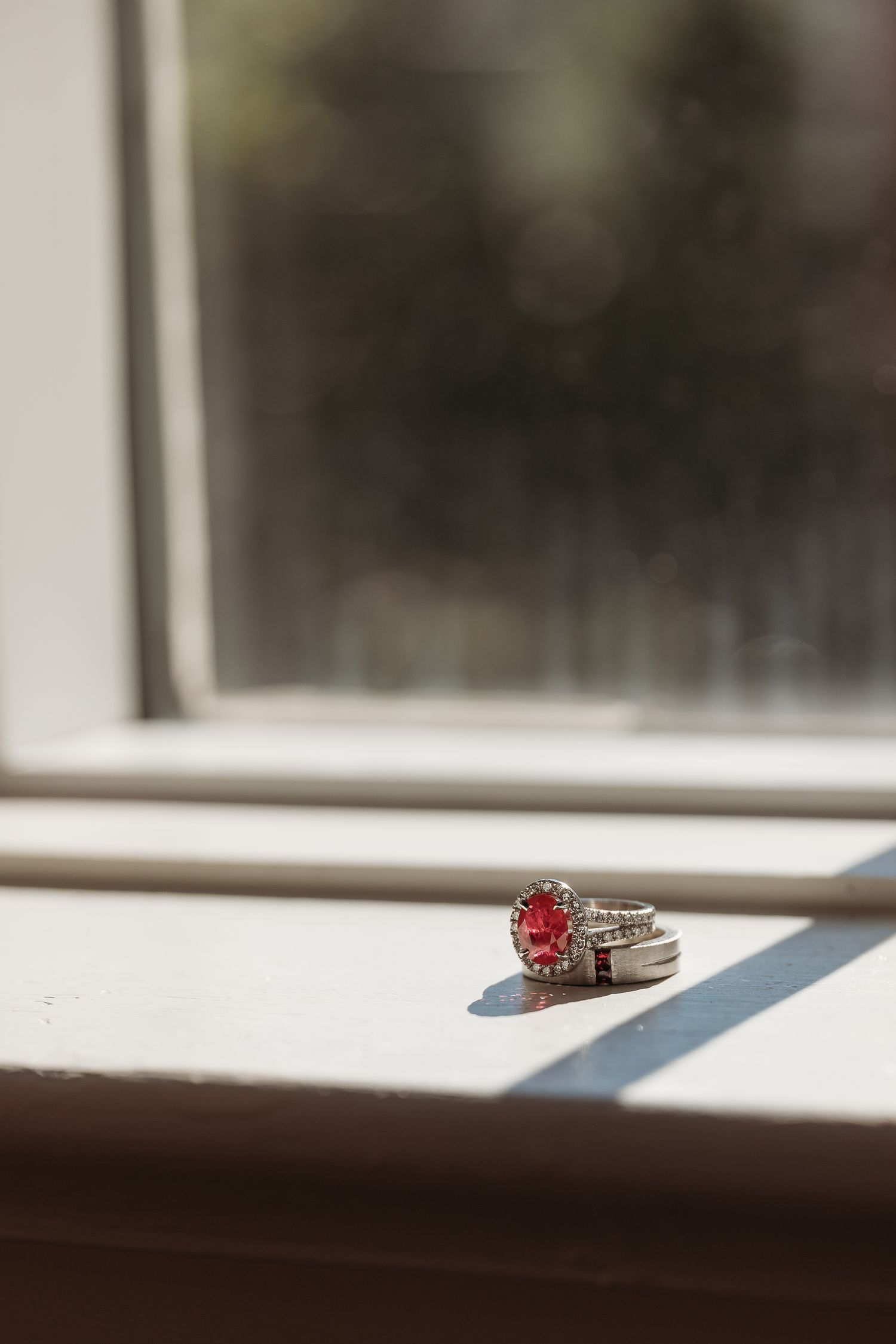 A gemstone ring sits on a white windowsill casting a long shadow in natural light.