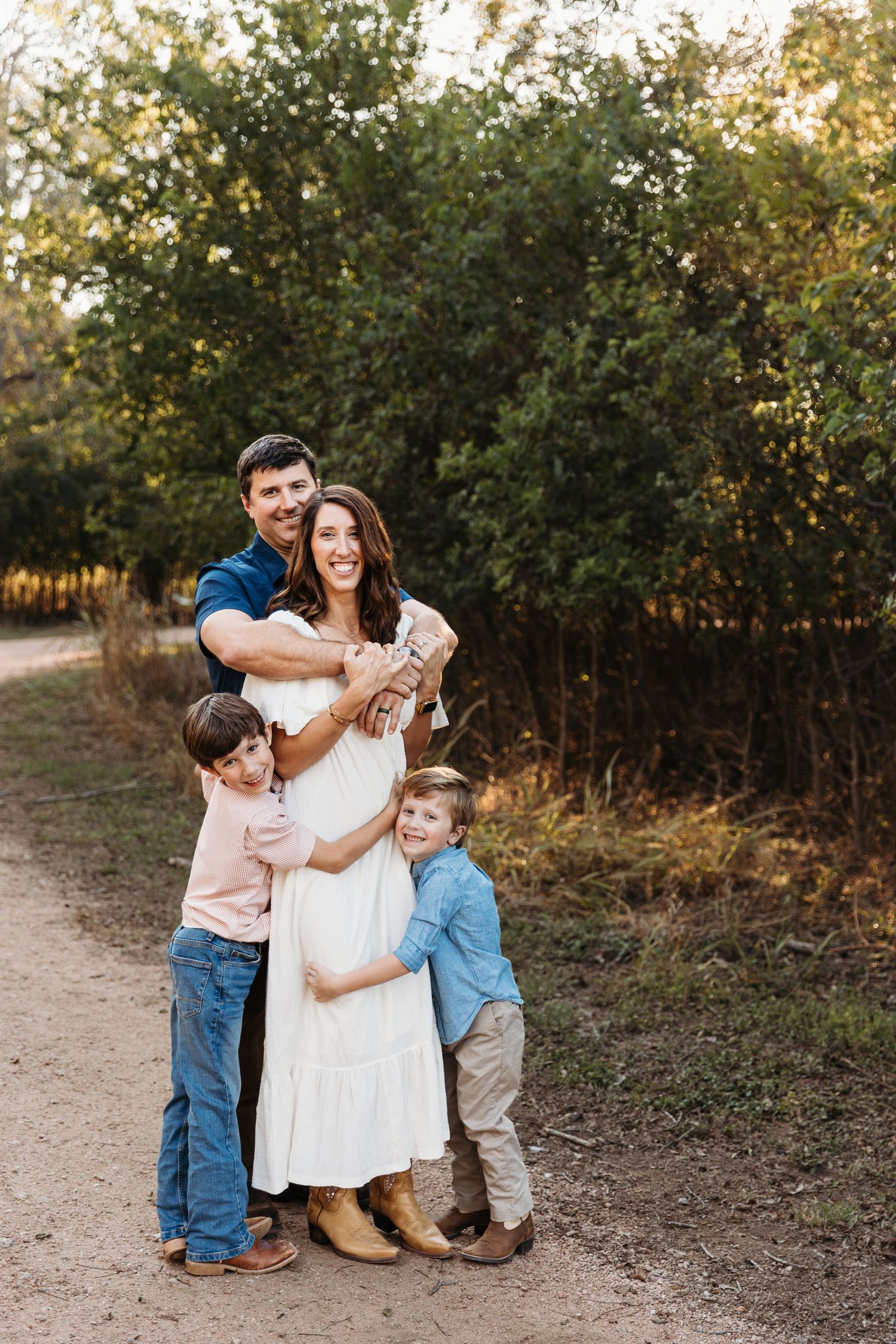A family shares tender moments together on a dirt path surrounded by autumn foliage at golden hour.