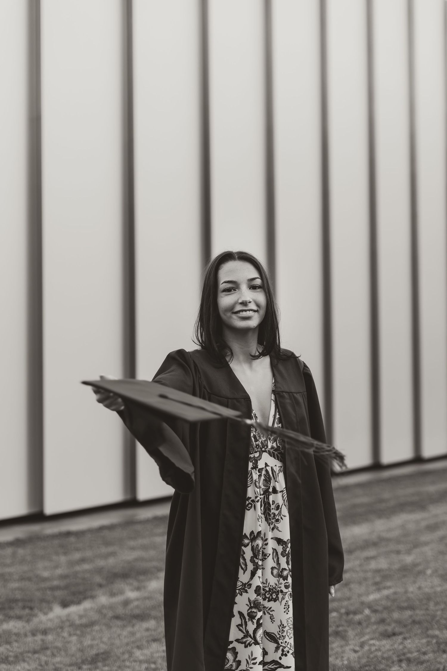 Graduate in blue cap and gown smiles while posing for graduation photos against a white striped wall.
