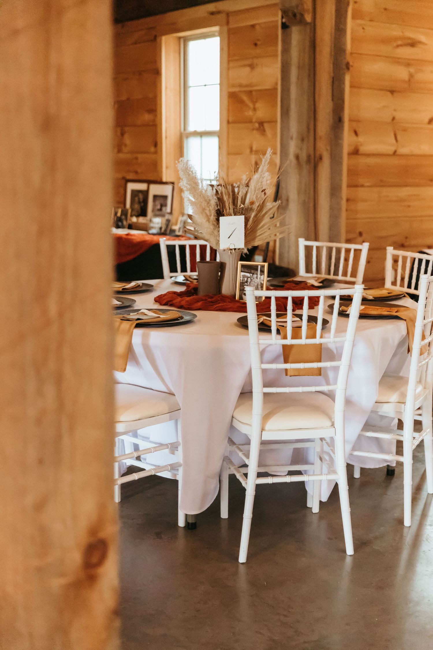 Modern rustic wedding venue interior with white chairs, string lights, and wooden beams in an elegant barn setting.