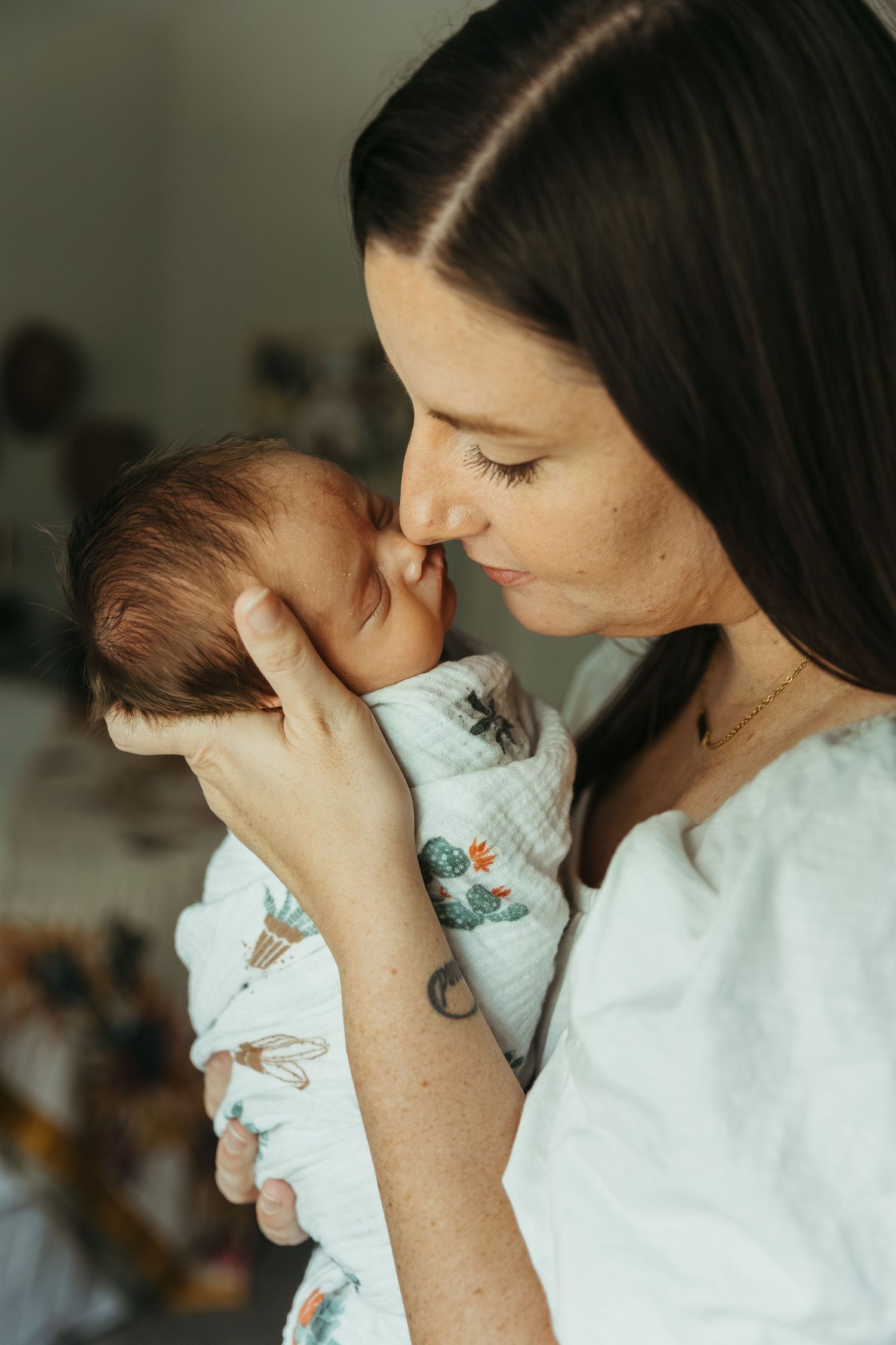 A tender moment between a mother and newborn baby as she gently cradles and kisses the infant in soft lighting.