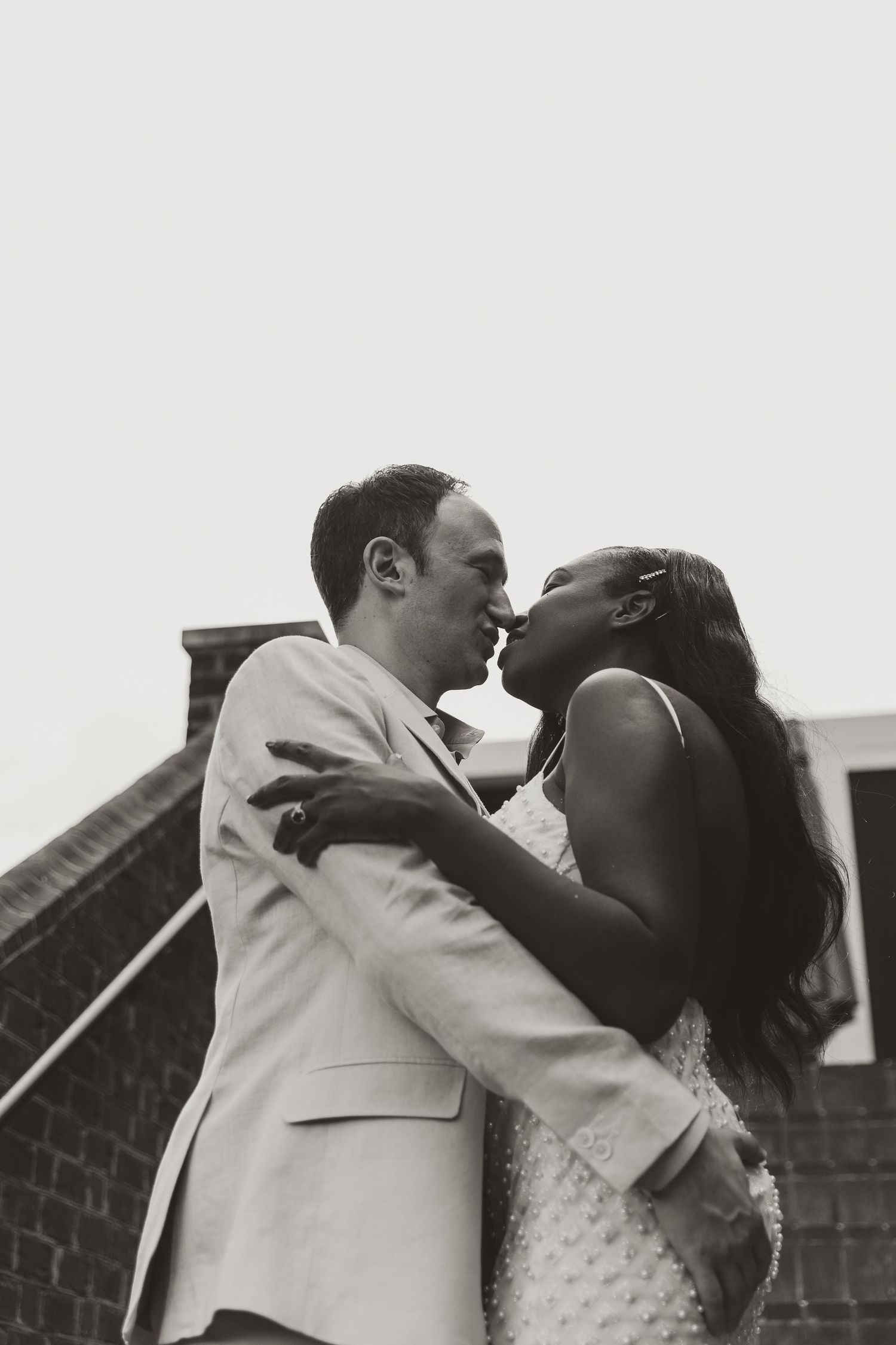 A romantic black and white wedding photo showing a couple sharing a tender kiss outdoors.