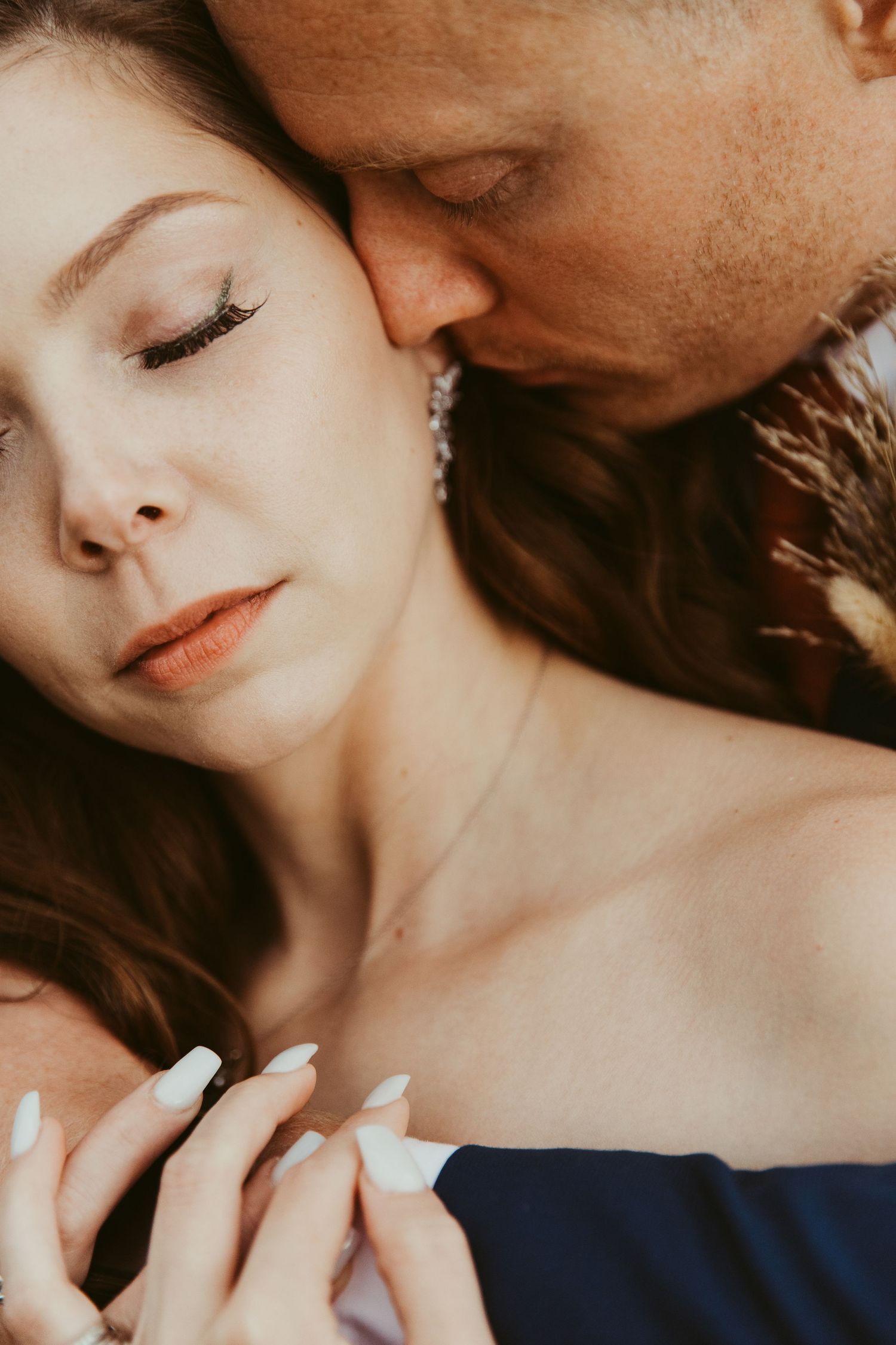 Romantic close-up portrait of couple embracing outdoors with hands clasped showing engagement ring.