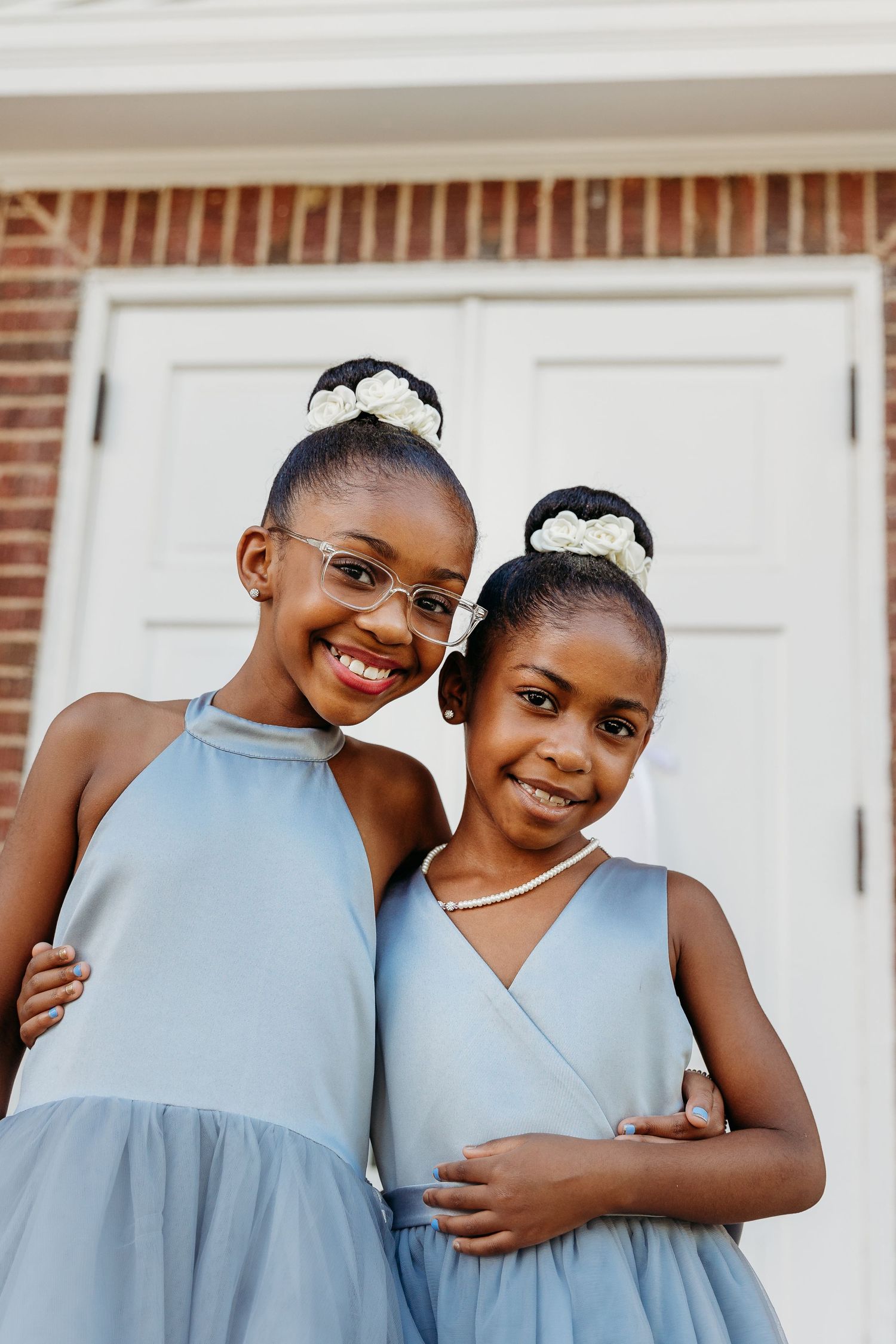 Two children in light blue and white outfits share affectionate embraces in a series of candid outdoor portraits.
