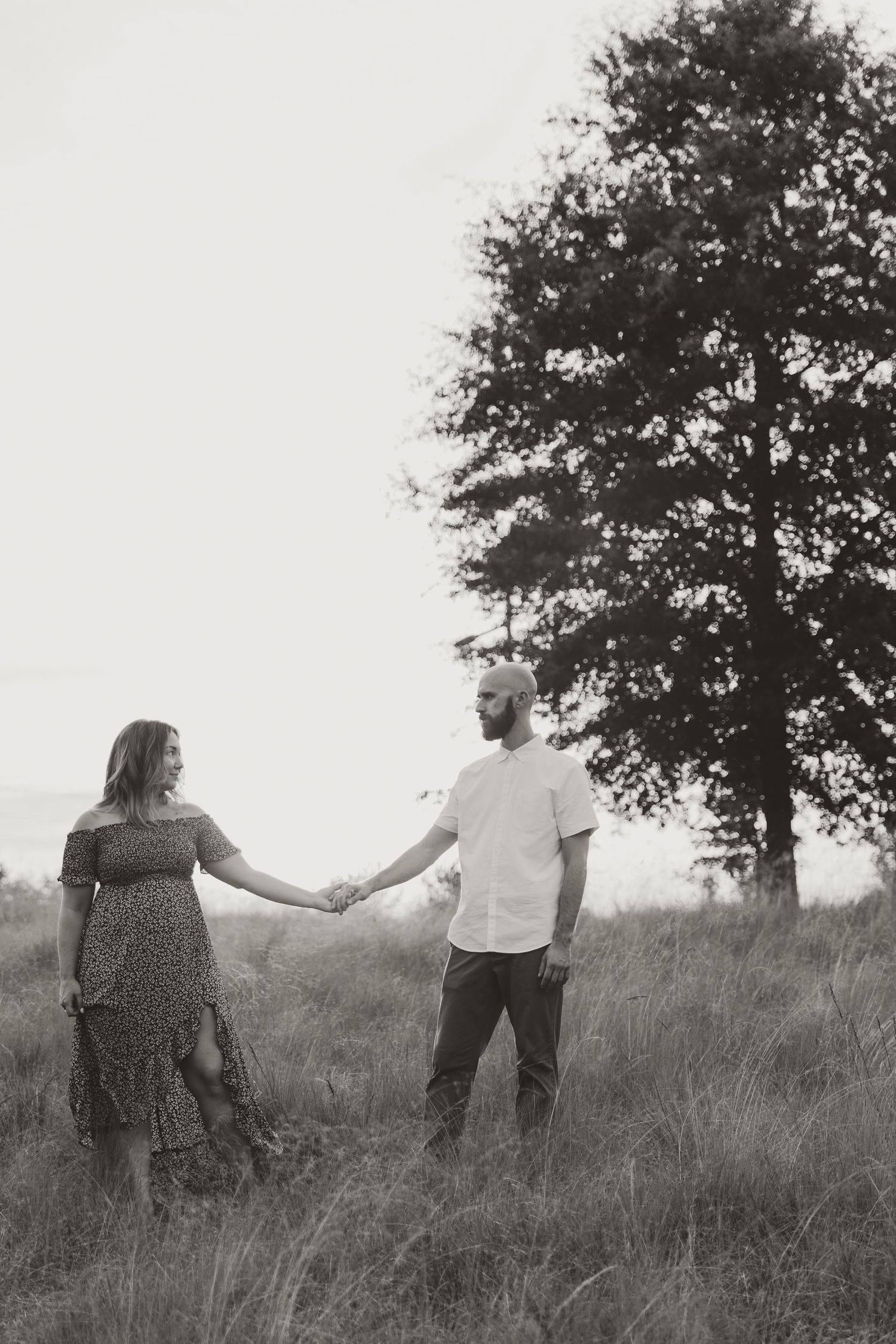 Black and white photo series showing a couple holding hands and walking through a misty field with trees in the background.