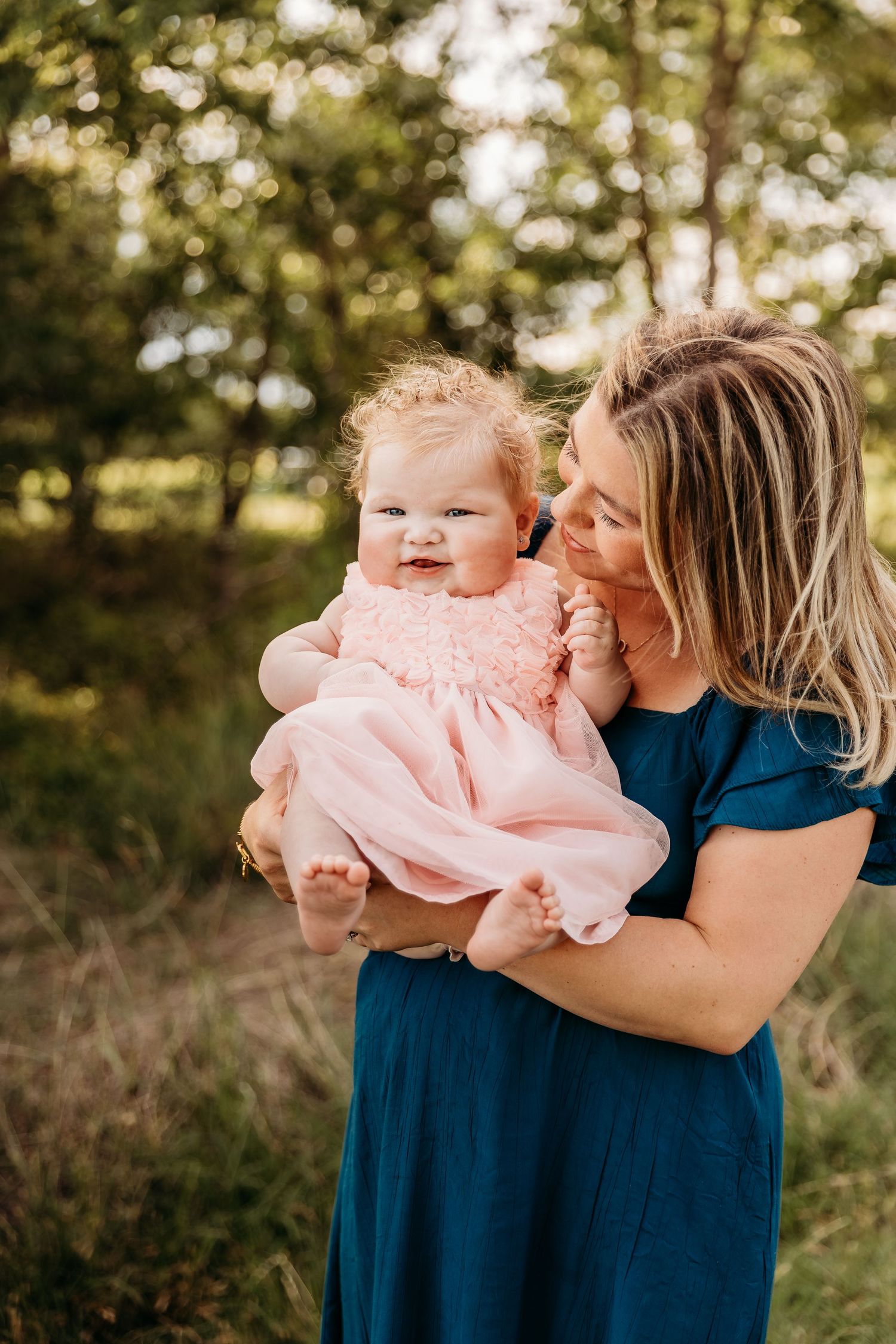 A parent in navy blue holds a baby wearing pink in a series of tender outdoor portrait photos at golden hour.