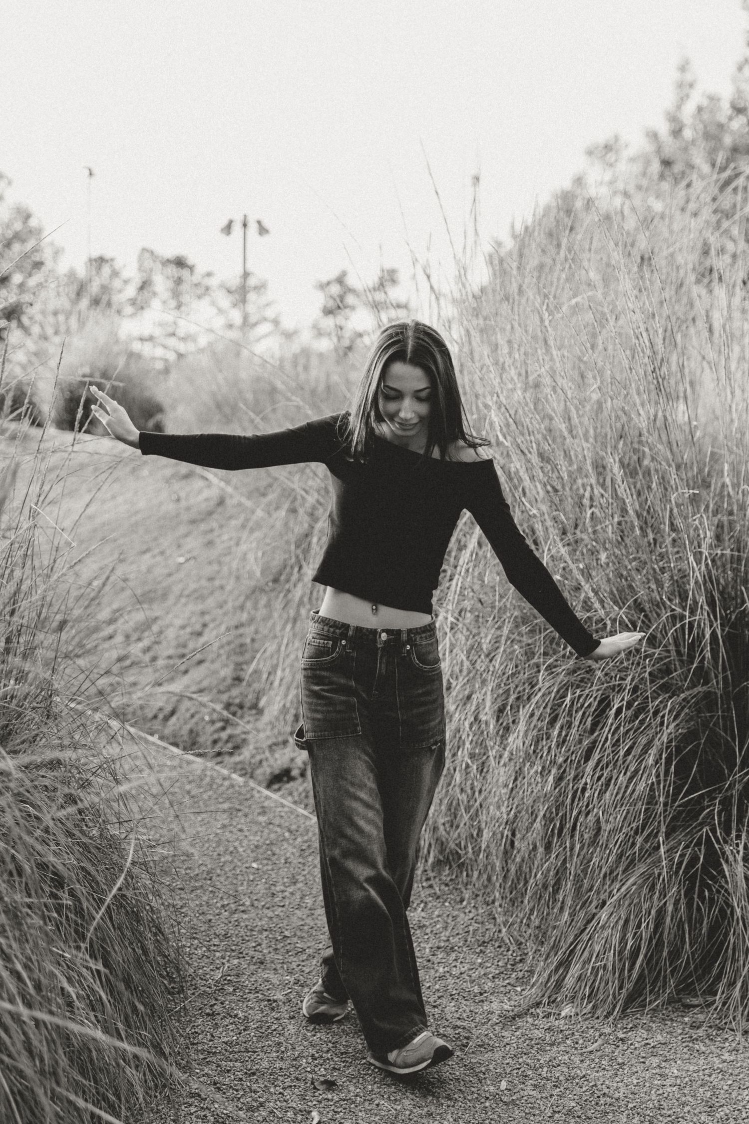 A person in dark clothing walks through tall grass in a black and white artistic photo series.