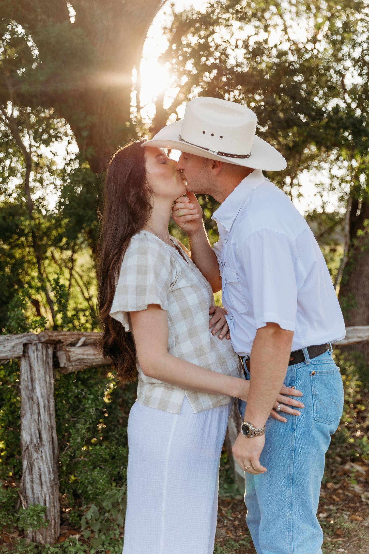 A couple in white and denim embrace and laugh together during a sunset photoshoot outdoors.