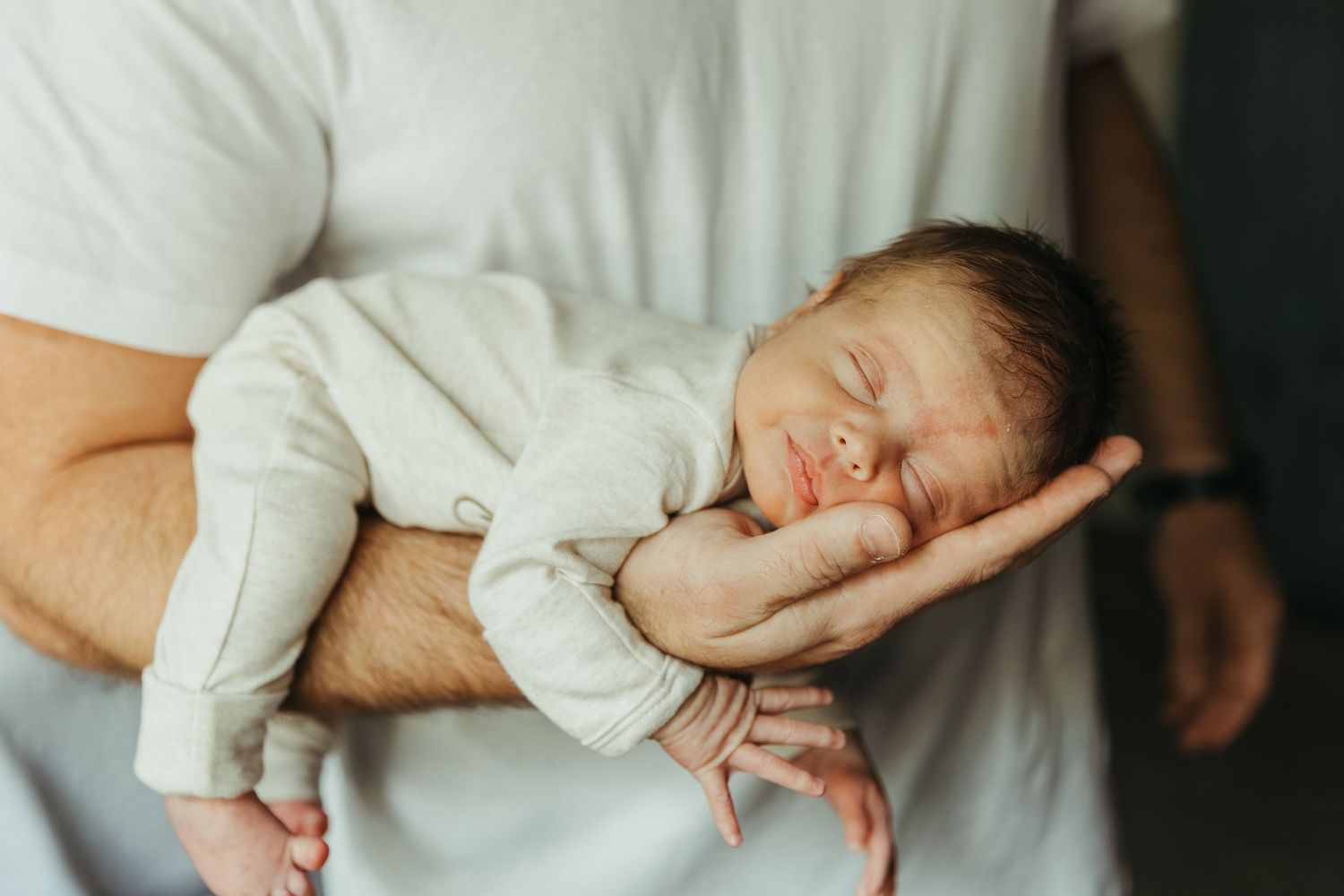 A series of connected images showing a newborn baby being held in various gentle positions against white bedding.
