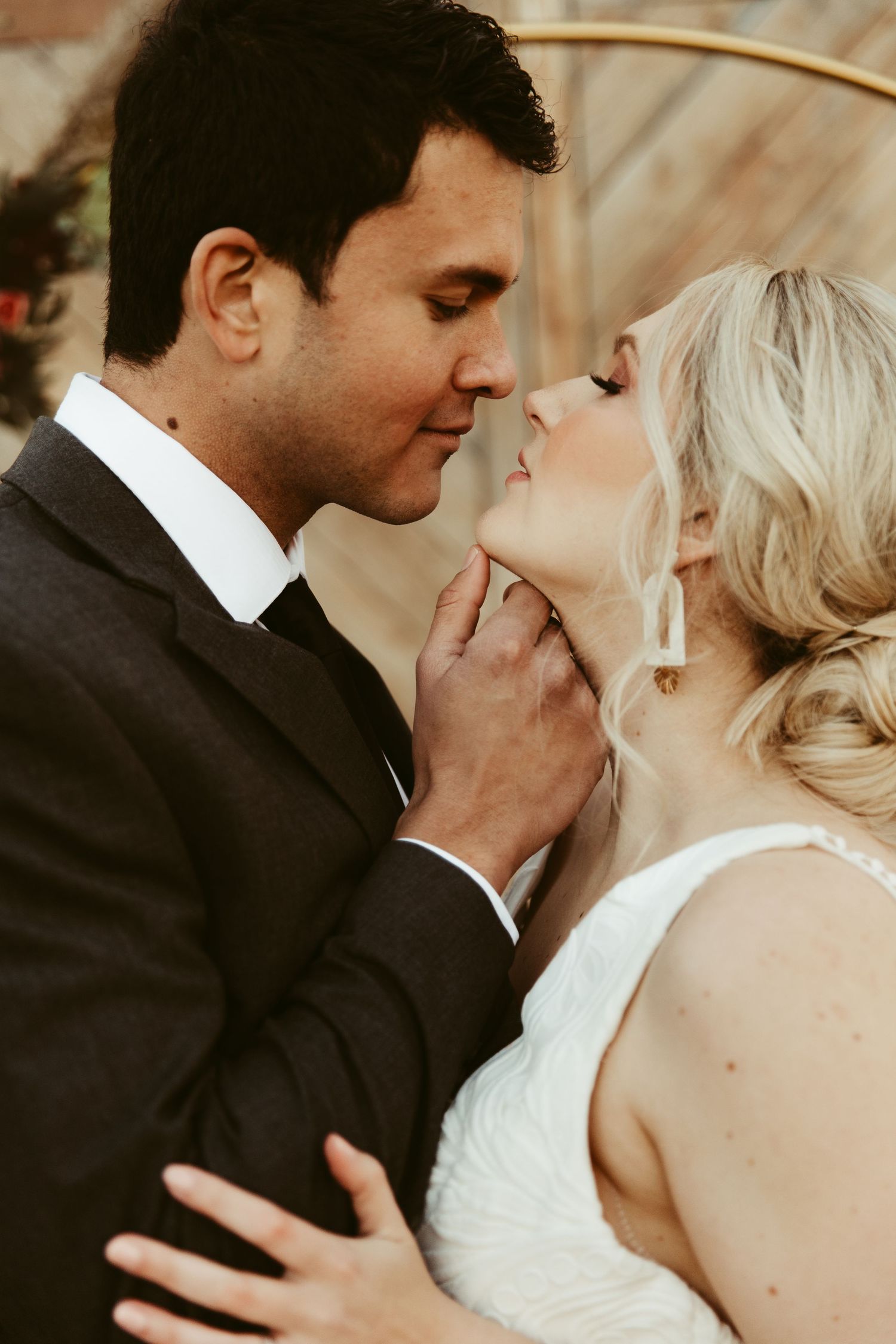 A romantic moment between newlyweds in front of a rustic wooden barn wall with floral decorations.