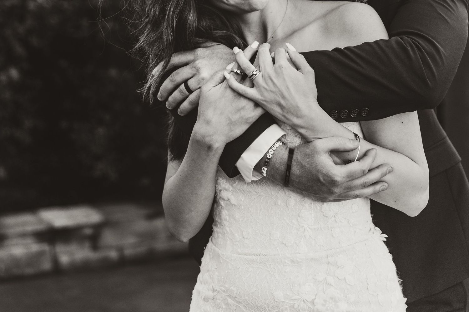 Black and white photo of couple embracing in wedding attire, with bride in white lace dress.