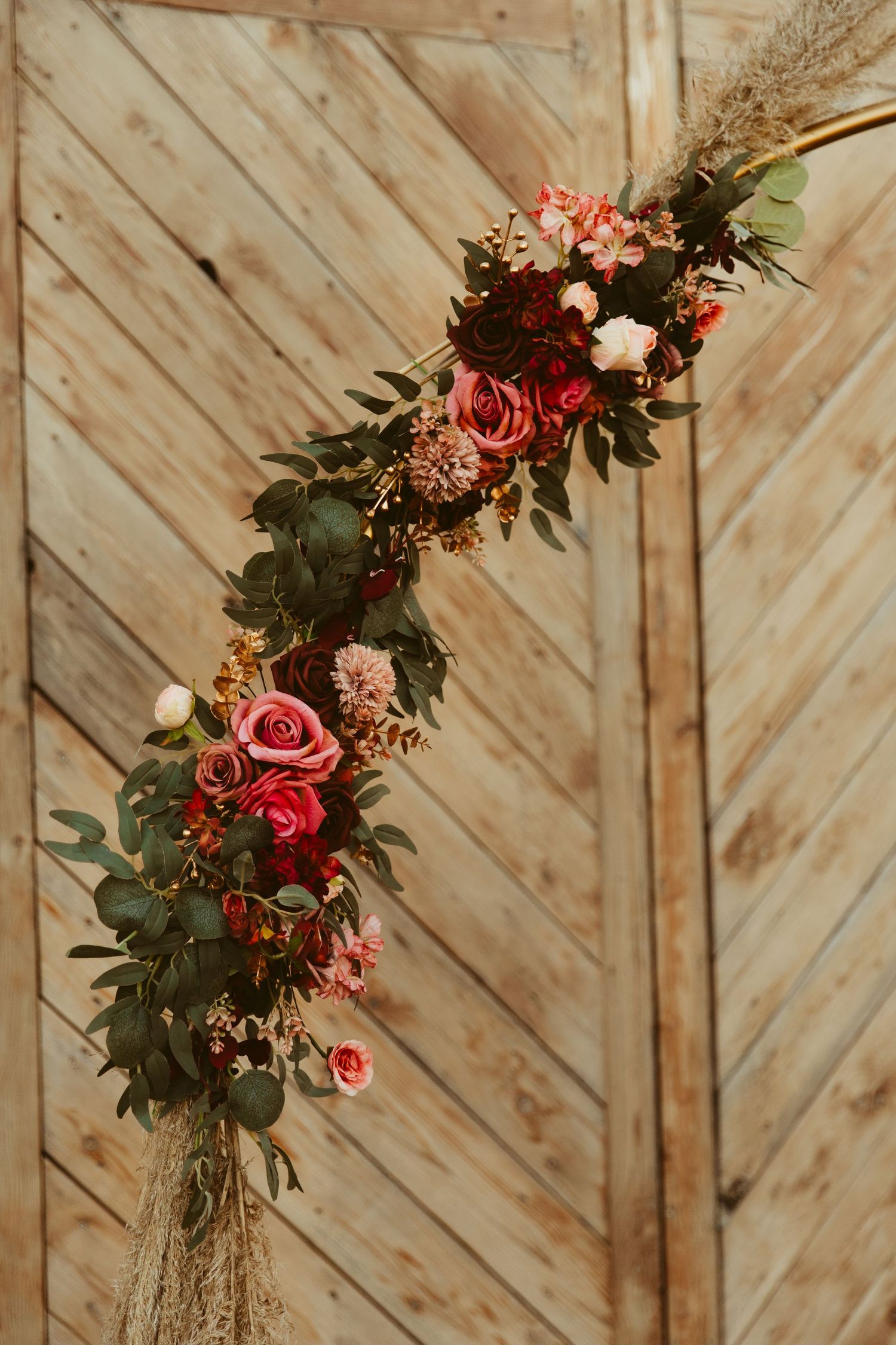 Beautiful floral arrangements with pink roses and greenery decorate a wooden chevron wall backdrop at an event.