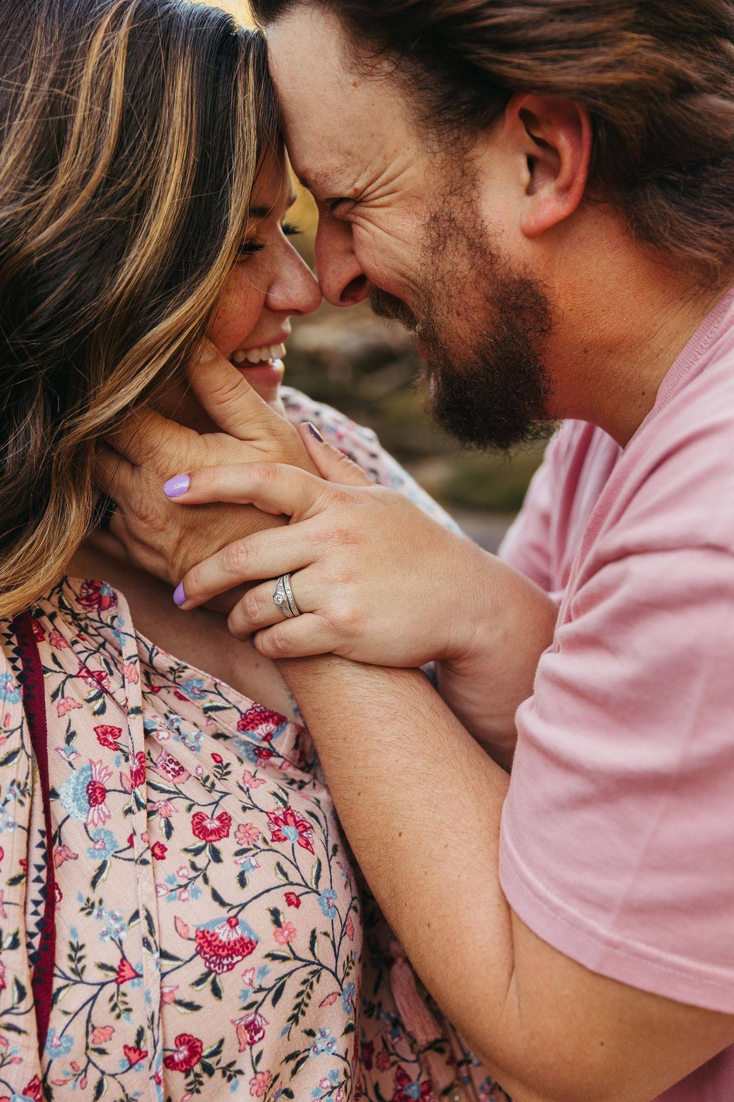 Romantic couple sharing an intimate moment outdoors, with woman in floral dress and man in pink shirt leaning close together.