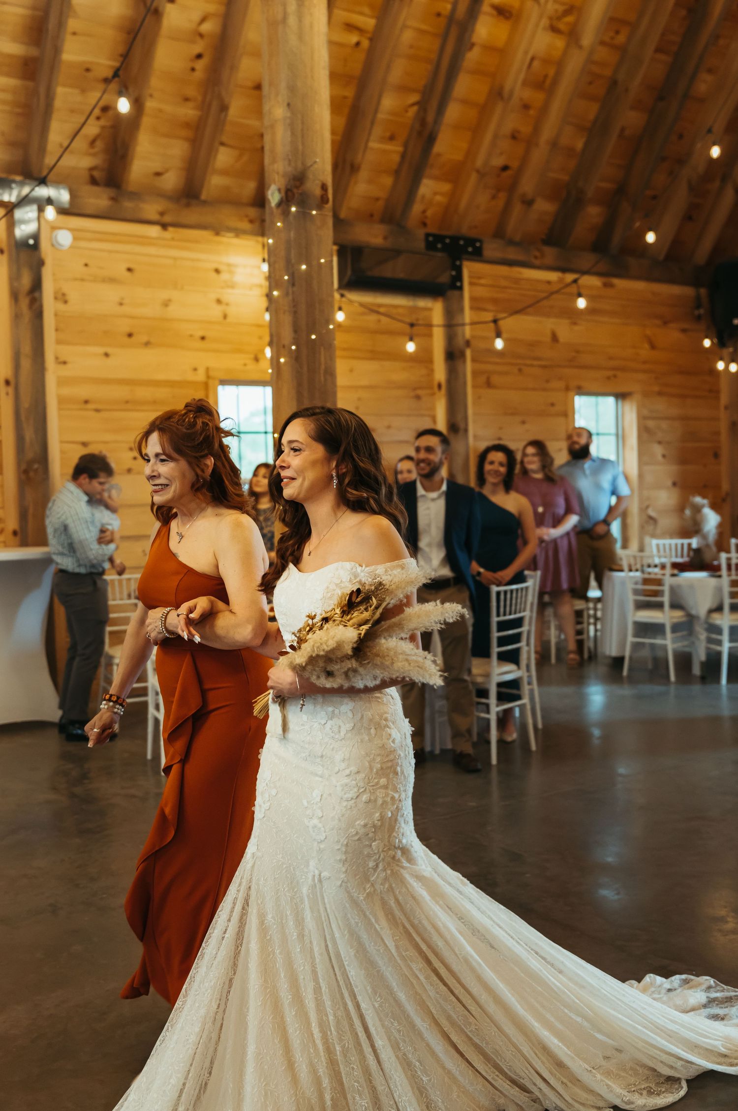 a woman in a rust dress walks her daughter in a wedding dress down the aisle
