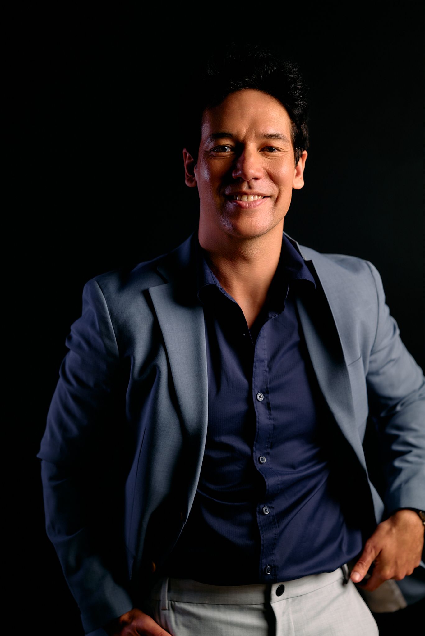 Professional studio portraits of someone in a dark blue suit against a black background with dramatic lighting.