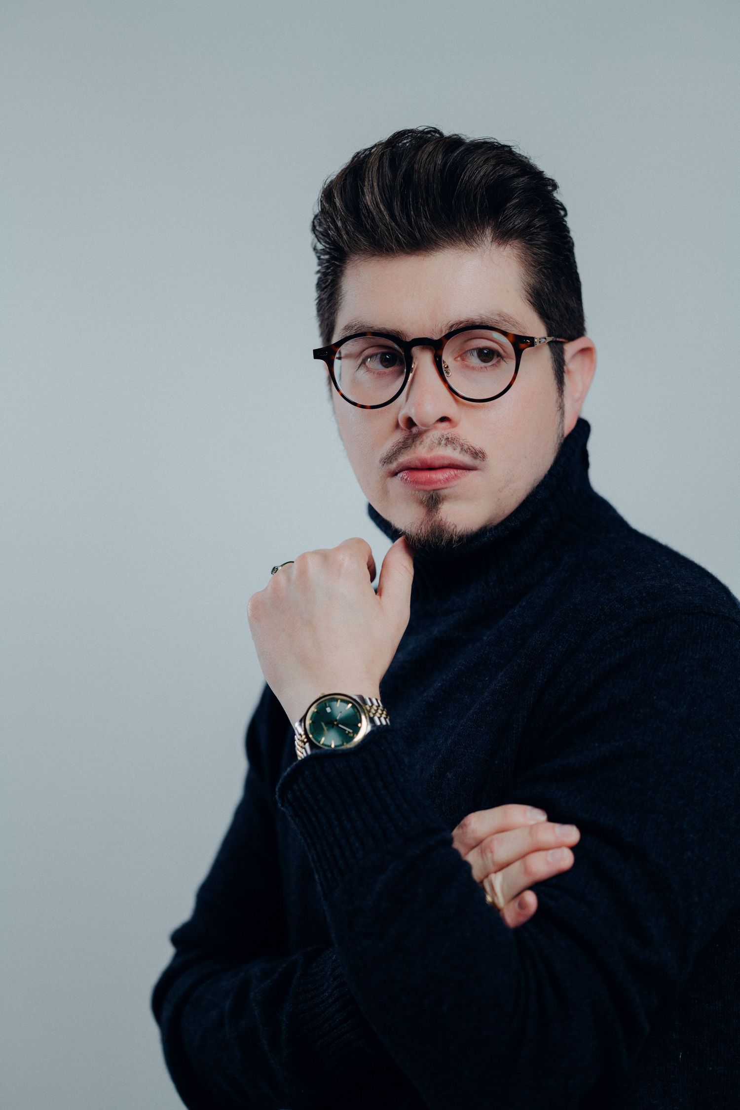 A series of artistic portrait shots showing a person in a black turtleneck and glasses against a light background.