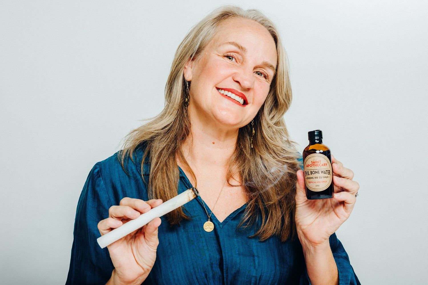 Woman smiling while holding various skincare and beauty products against white background.