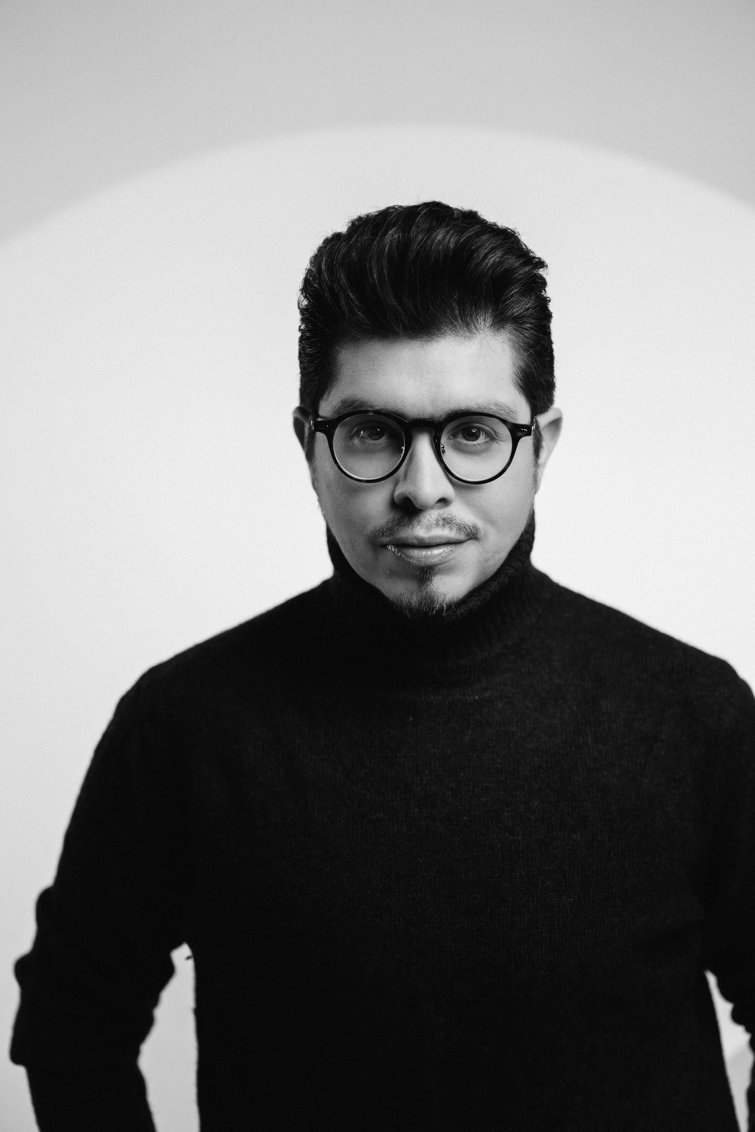 Black and white portrait of someone wearing glasses and a black turtleneck sweater against a light background.