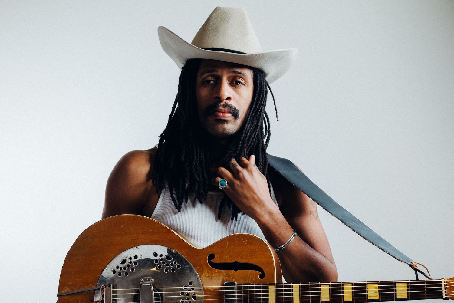 Musician with cowboy hat plays acoustic guitar against white background.