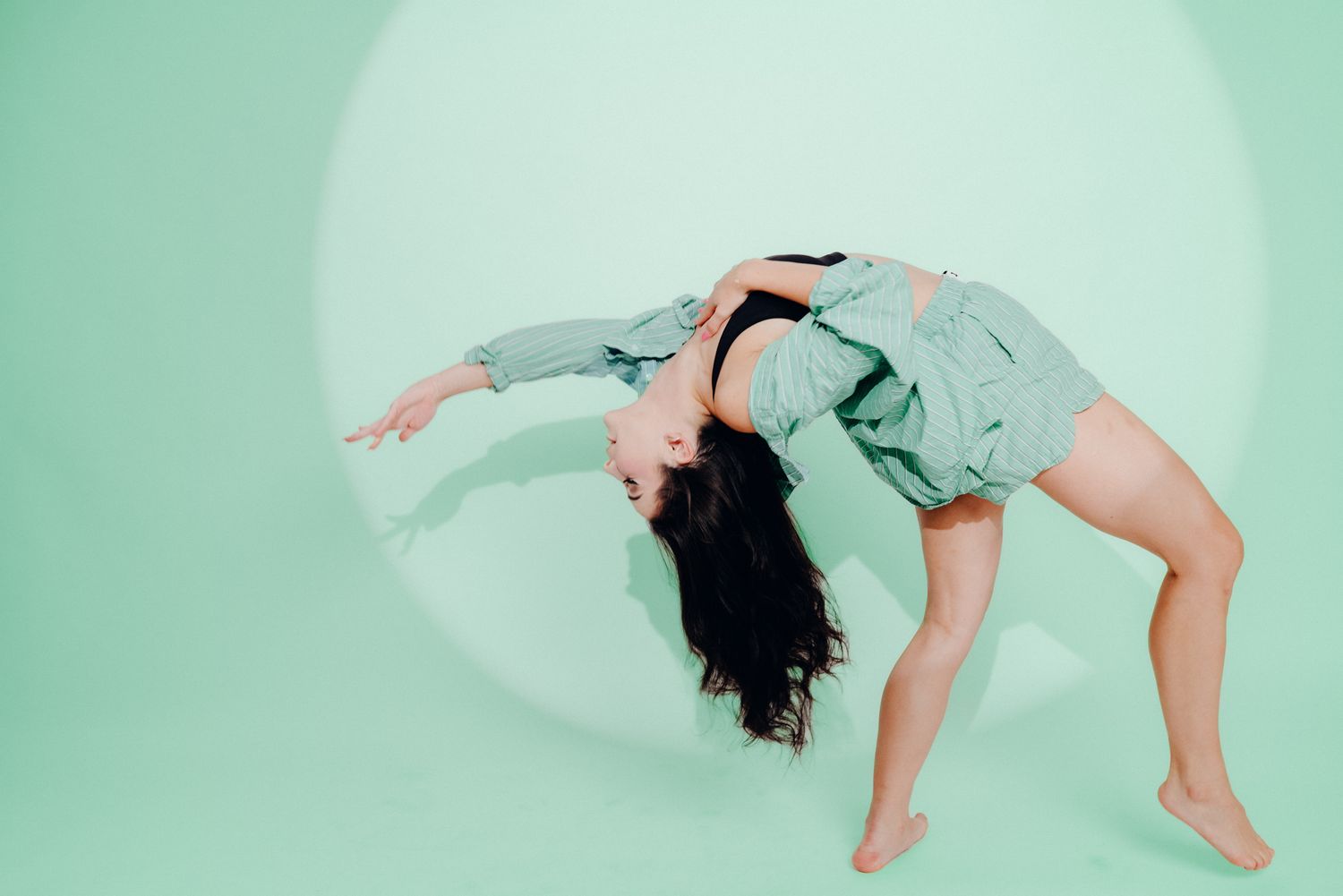 Contemporary dancer performs fluid movements in black outfit against mint green background.