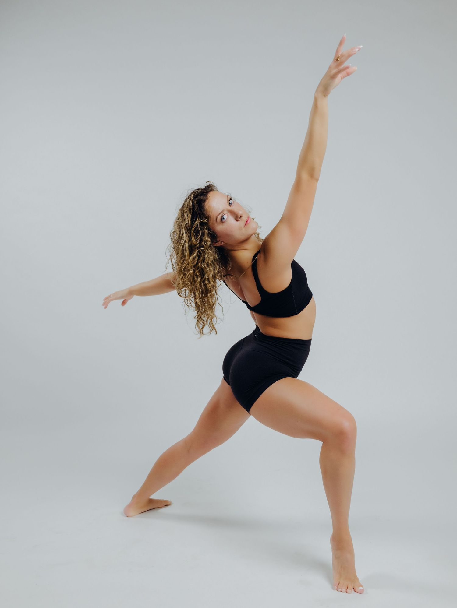 Dancer in black athletic wear performs graceful contemporary dance movements against light gray background.