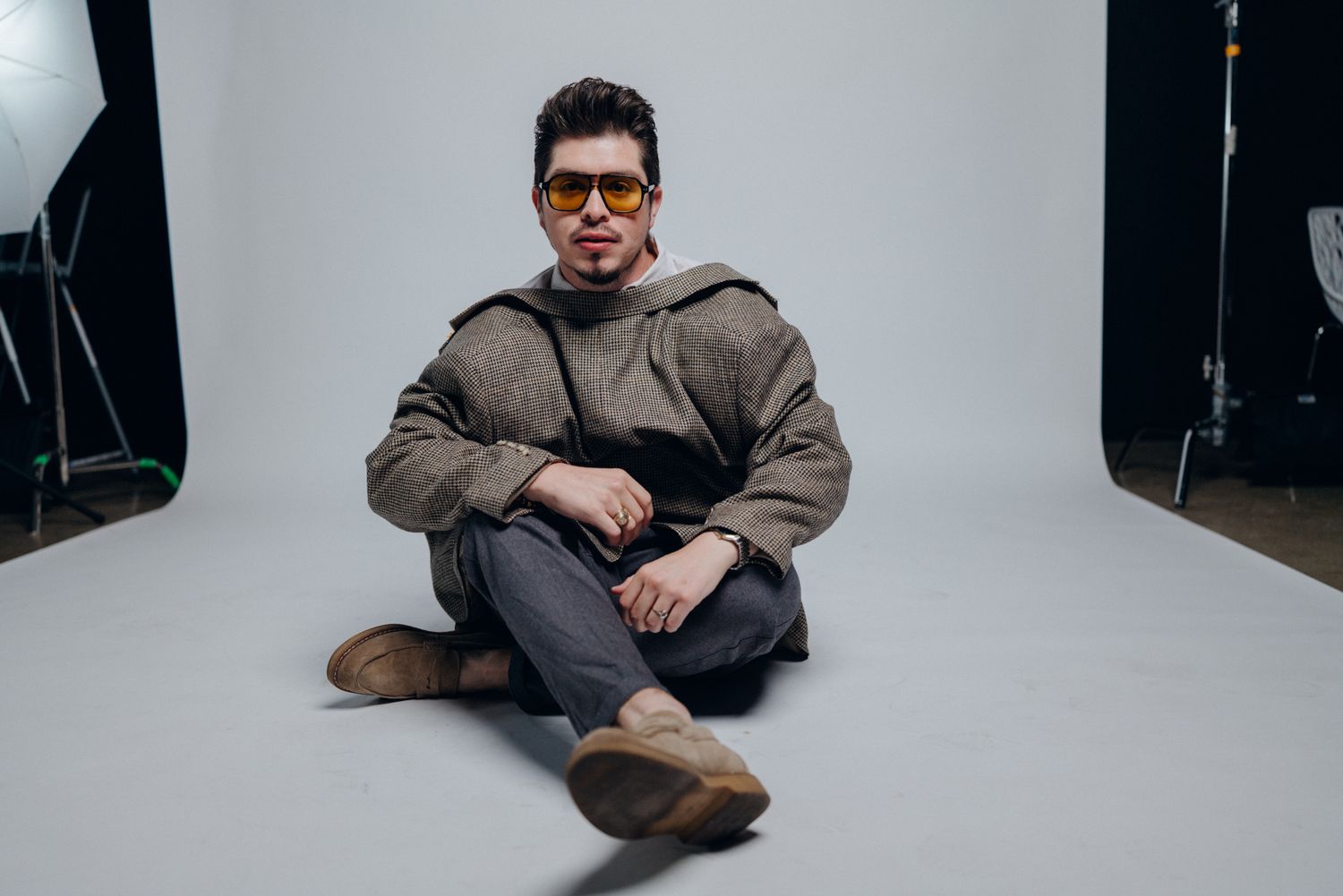 Person in casual brown outfit and glasses sits on floor against white wall in various relaxed poses.