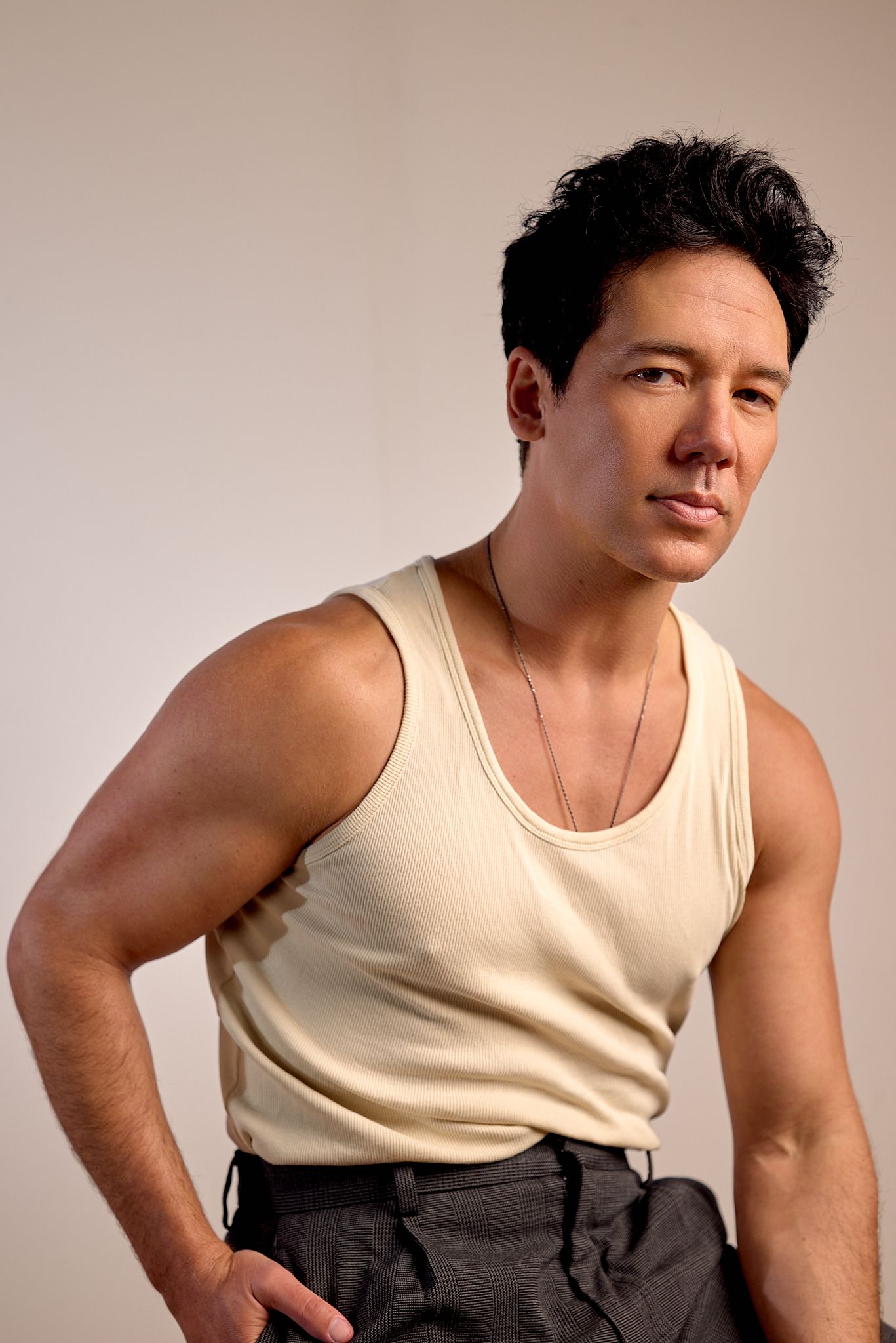 Person in cream tank top and dark pants poses in sequence against neutral backdrop.