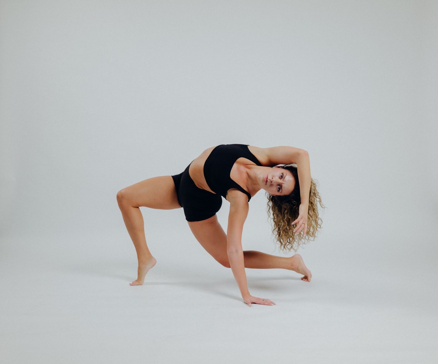 Modern dancer performs floor choreography in black athletic wear against neutral background.