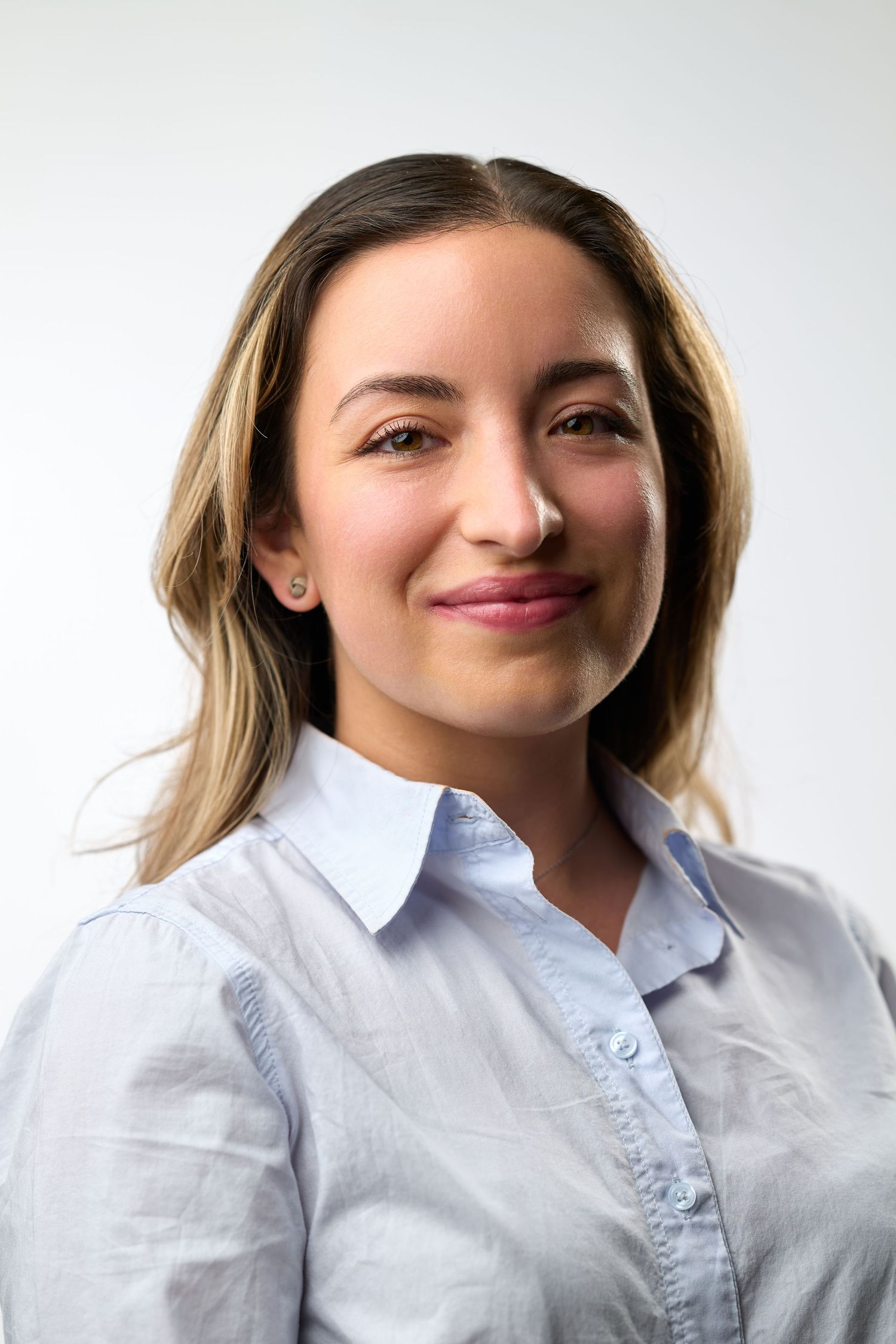 Person in white button-up shirt smiling warmly against light background in professional headshot series.