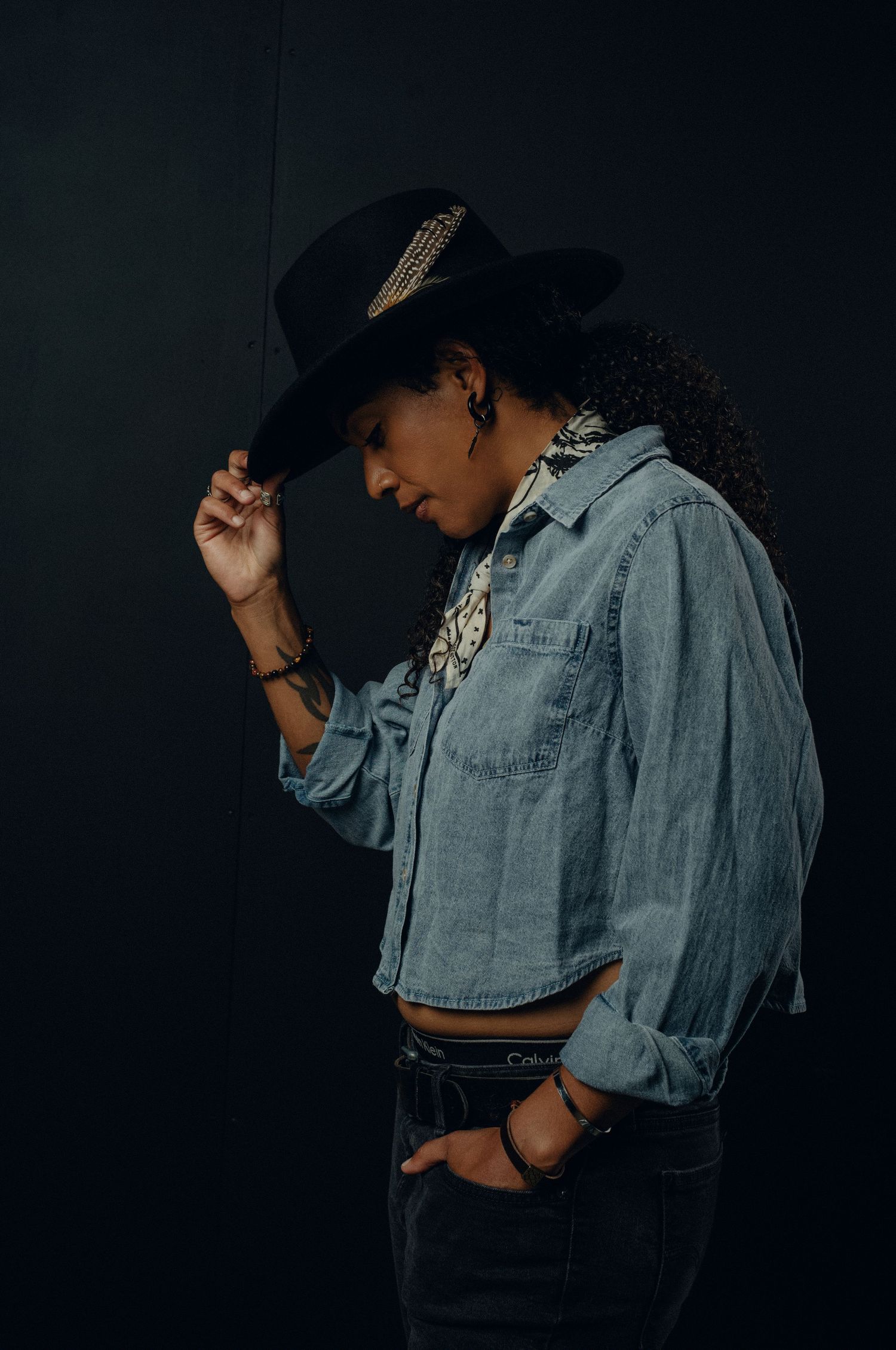 A person in a denim jacket poses dramatically against a dark background in a series of moody portrait shots.