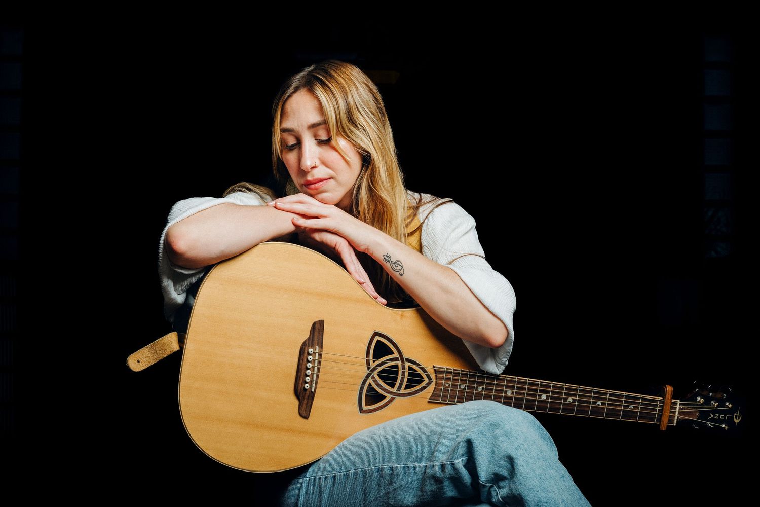 Person playing acoustic guitar in dramatic lighting against dark background.