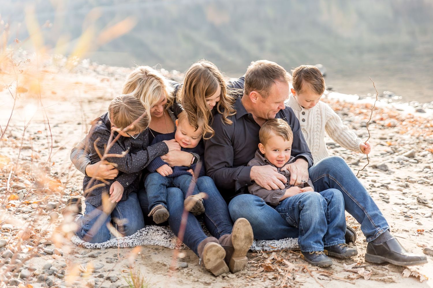 Family sitting together on autumn ground covered in fallen leaves wearing coordinated navy outfits.