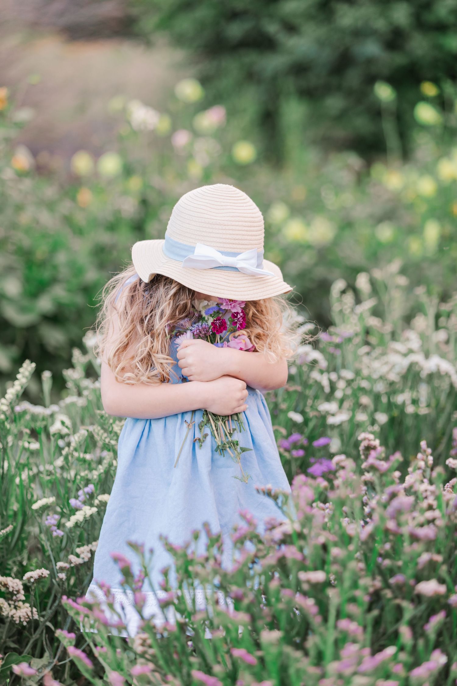 Young girl in blue dress picking wildflowers in a meadow on a sunny day.