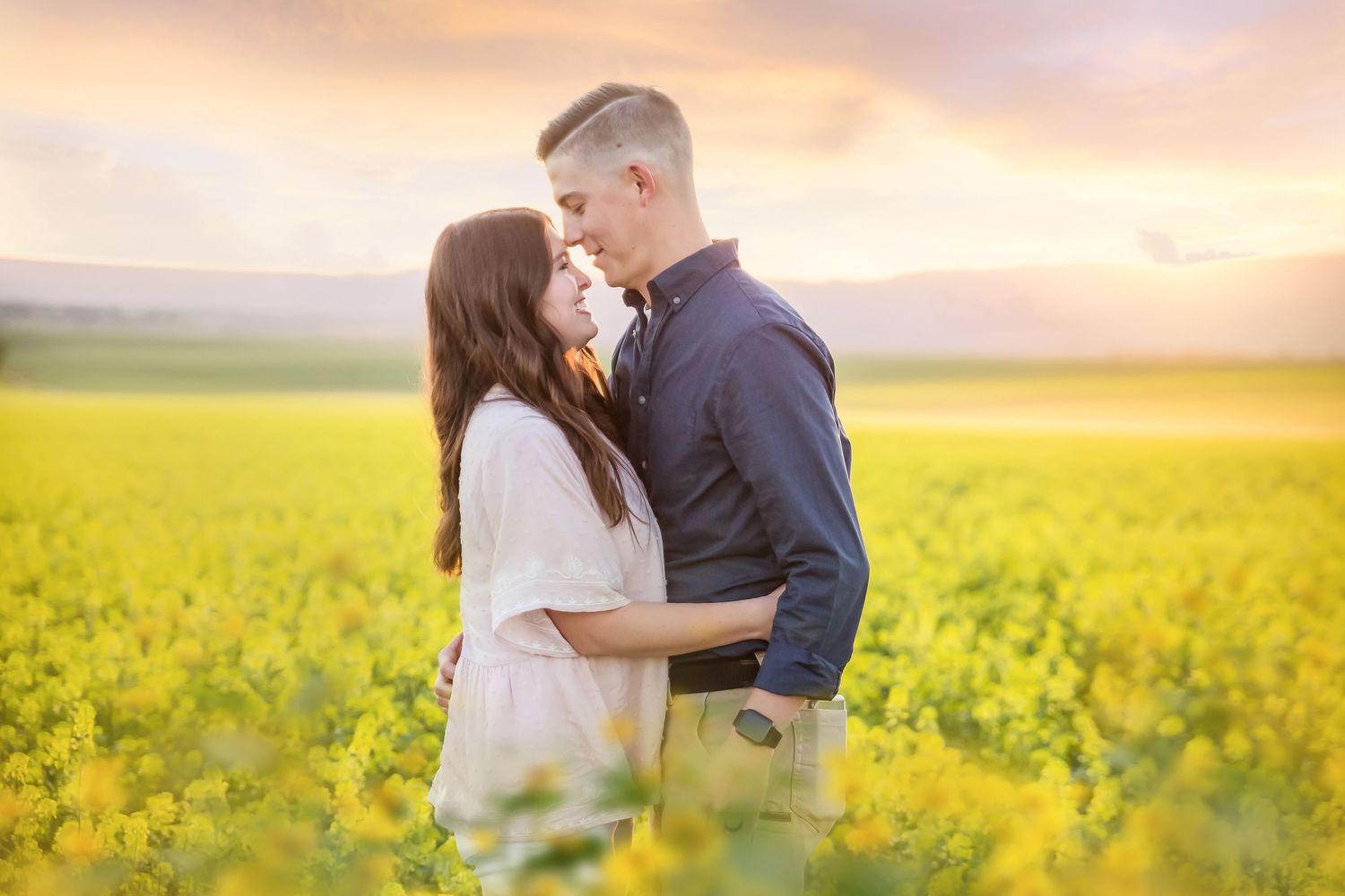 Romantic couple embracing in golden canola field during sunset.