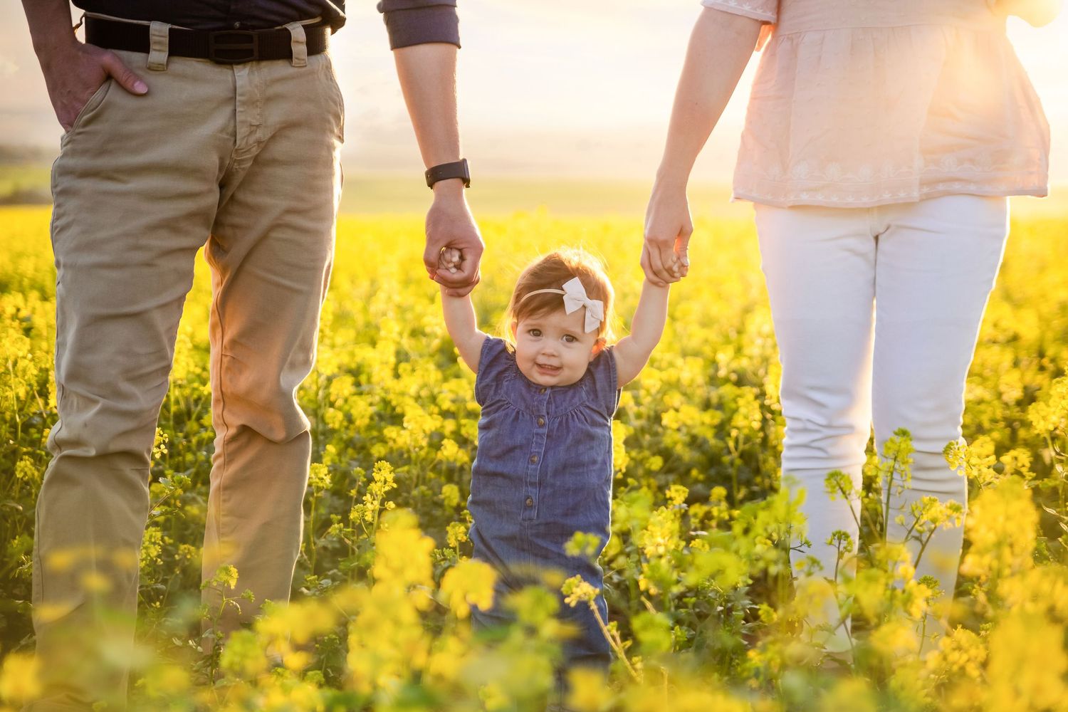 Lower body view of family standing together in blooming yellow canola field.