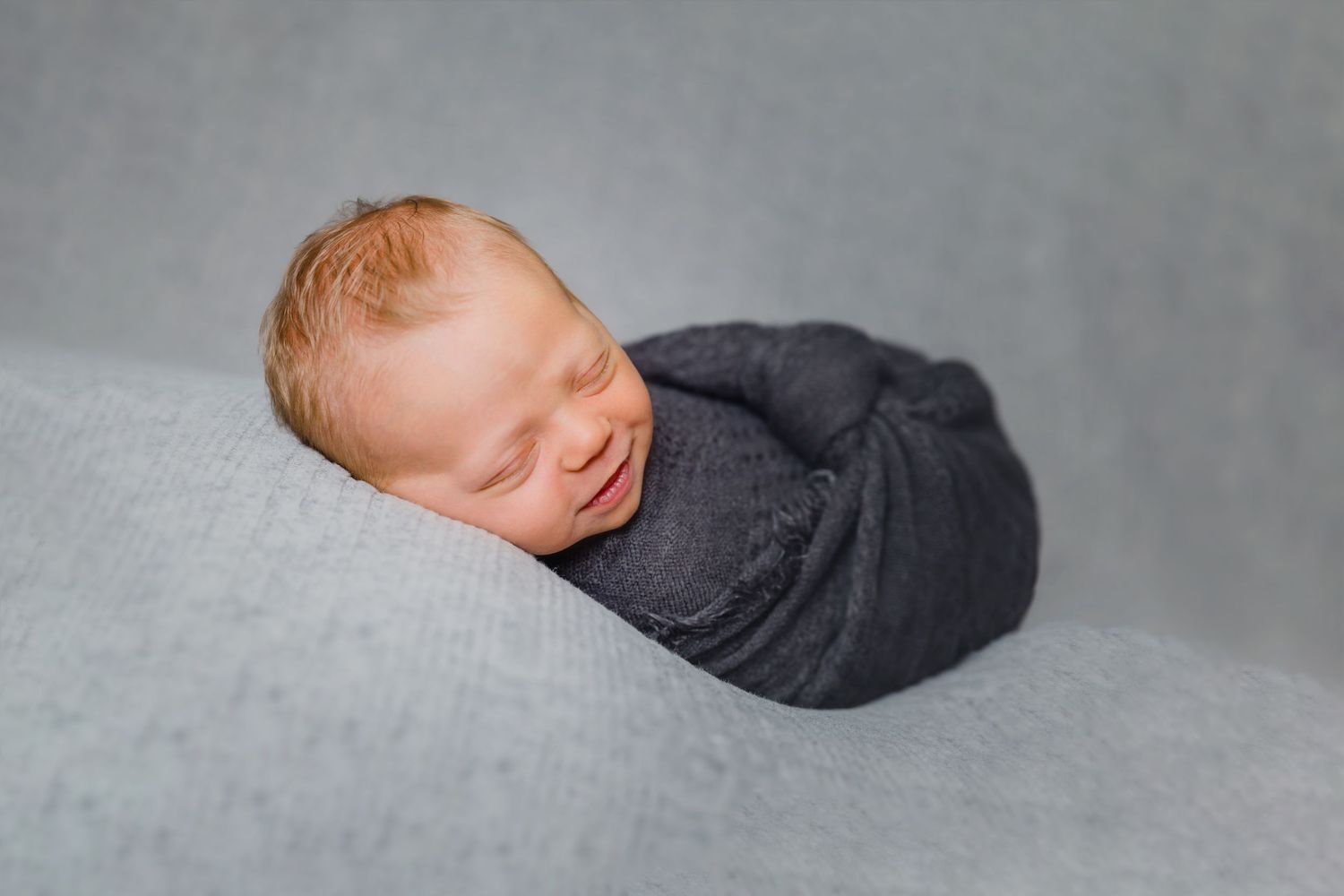Close-up newborn photography with soft gray textures and gentle lighting creating a peaceful sleeping portrait.