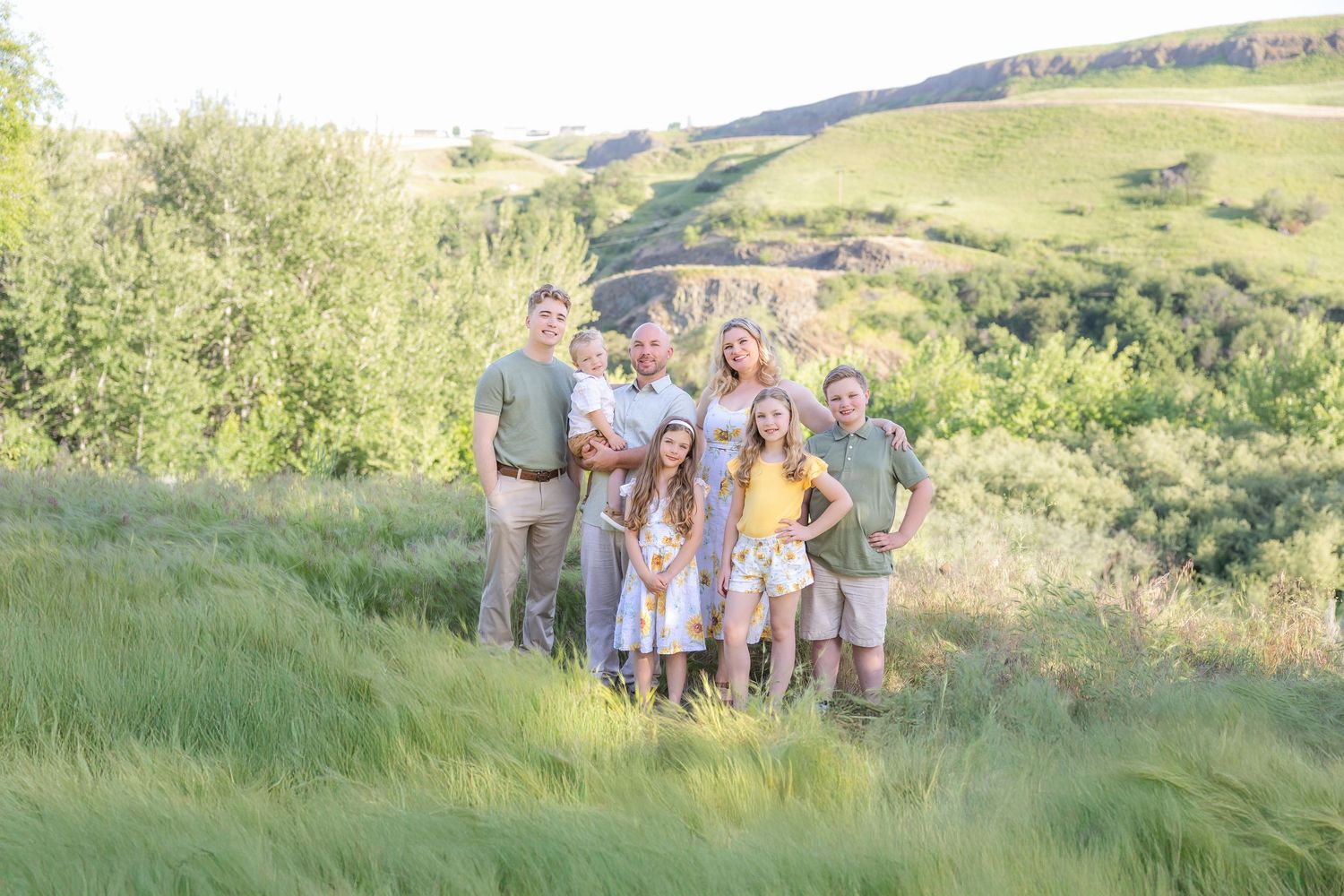 A group poses together on a grassy hillside wearing coordinated neutral-toned outfits during a sunny outdoor photoshoot.